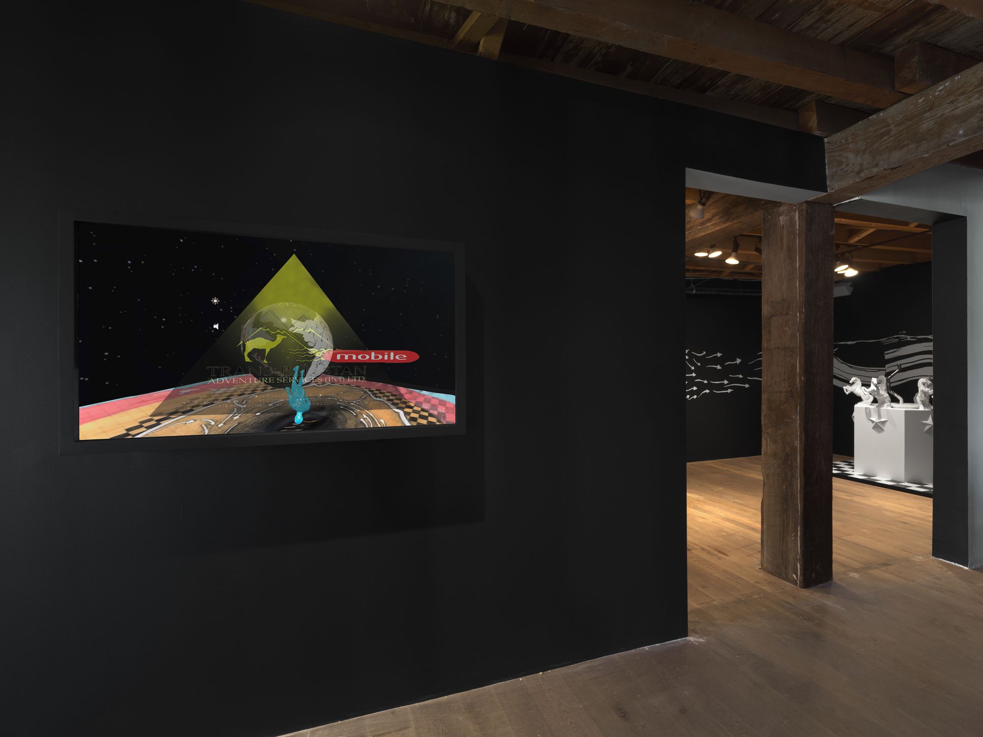 A wide angle view of the entrance to the exhibition, with a video piece hung on the wall to the left of the gallery entrance.