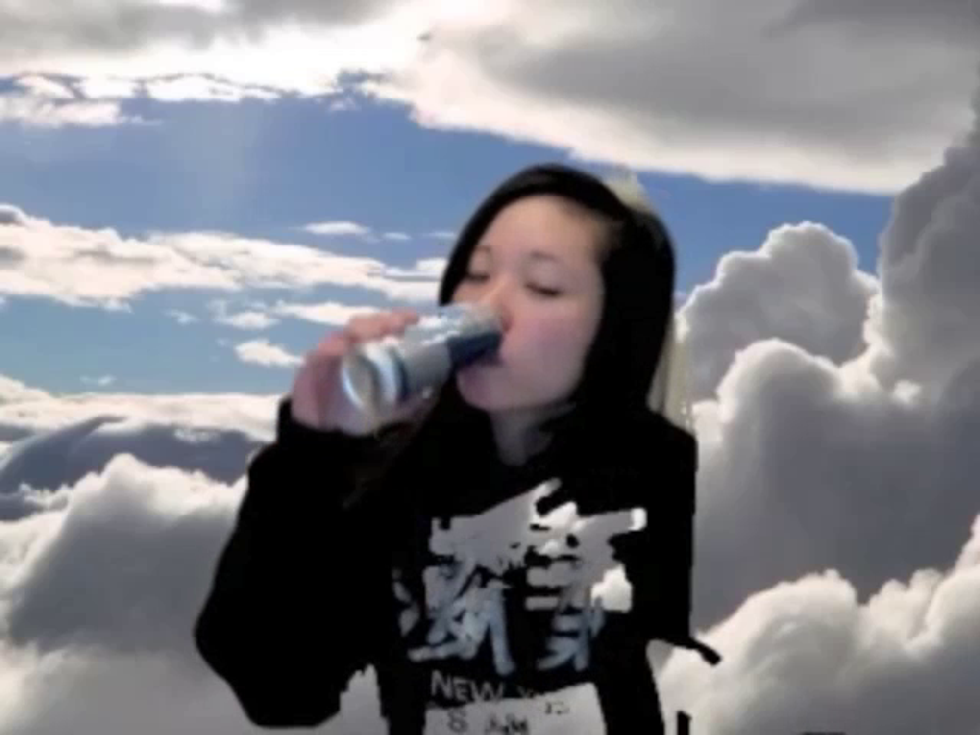 A webcam still with a woman wearing a black and white long sleeve shirt drinking a Red Bull with a sky and clouds background