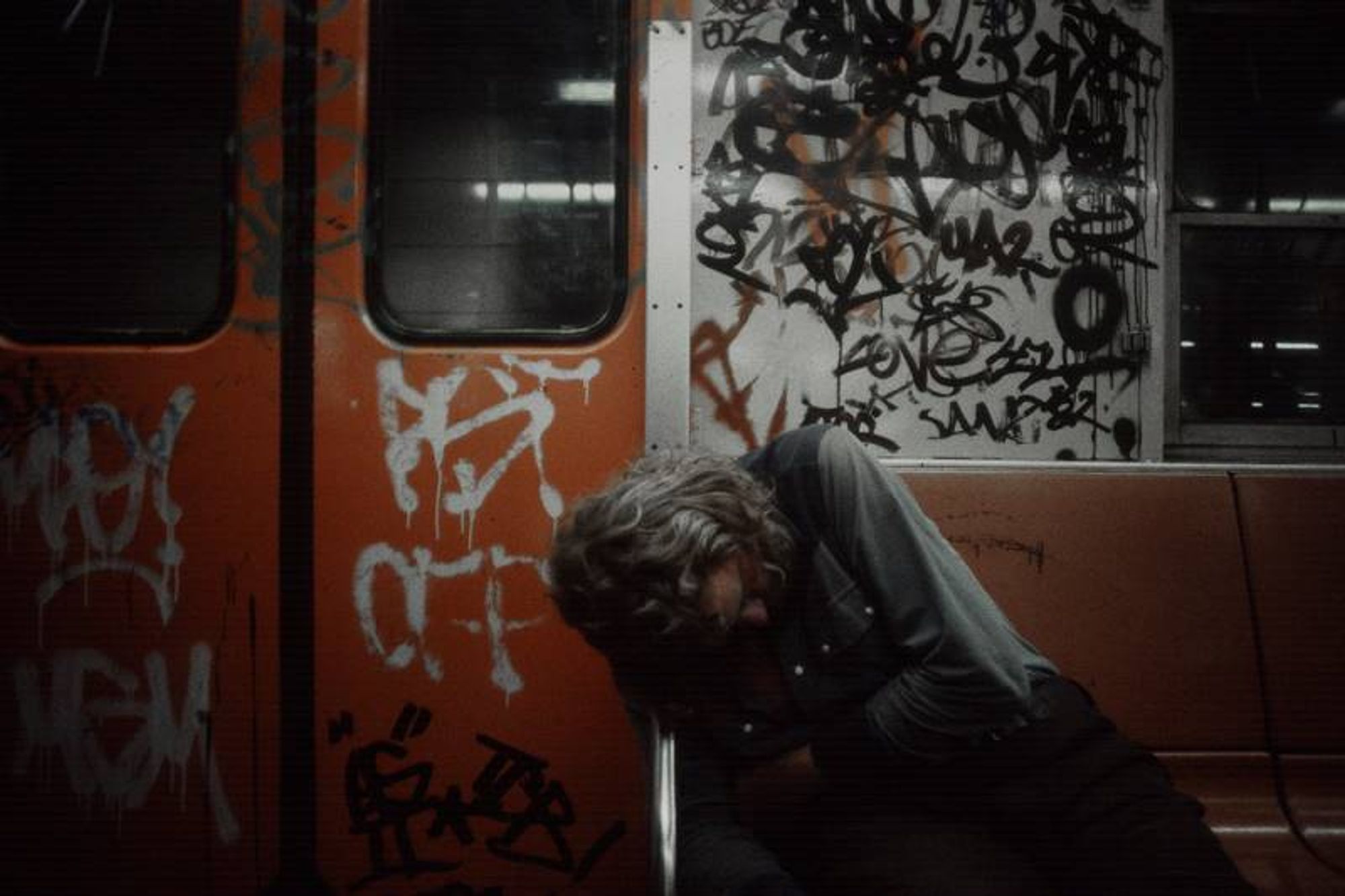 Photo of a man passed out on the subway in the 90s, the car covered with graffiti. 