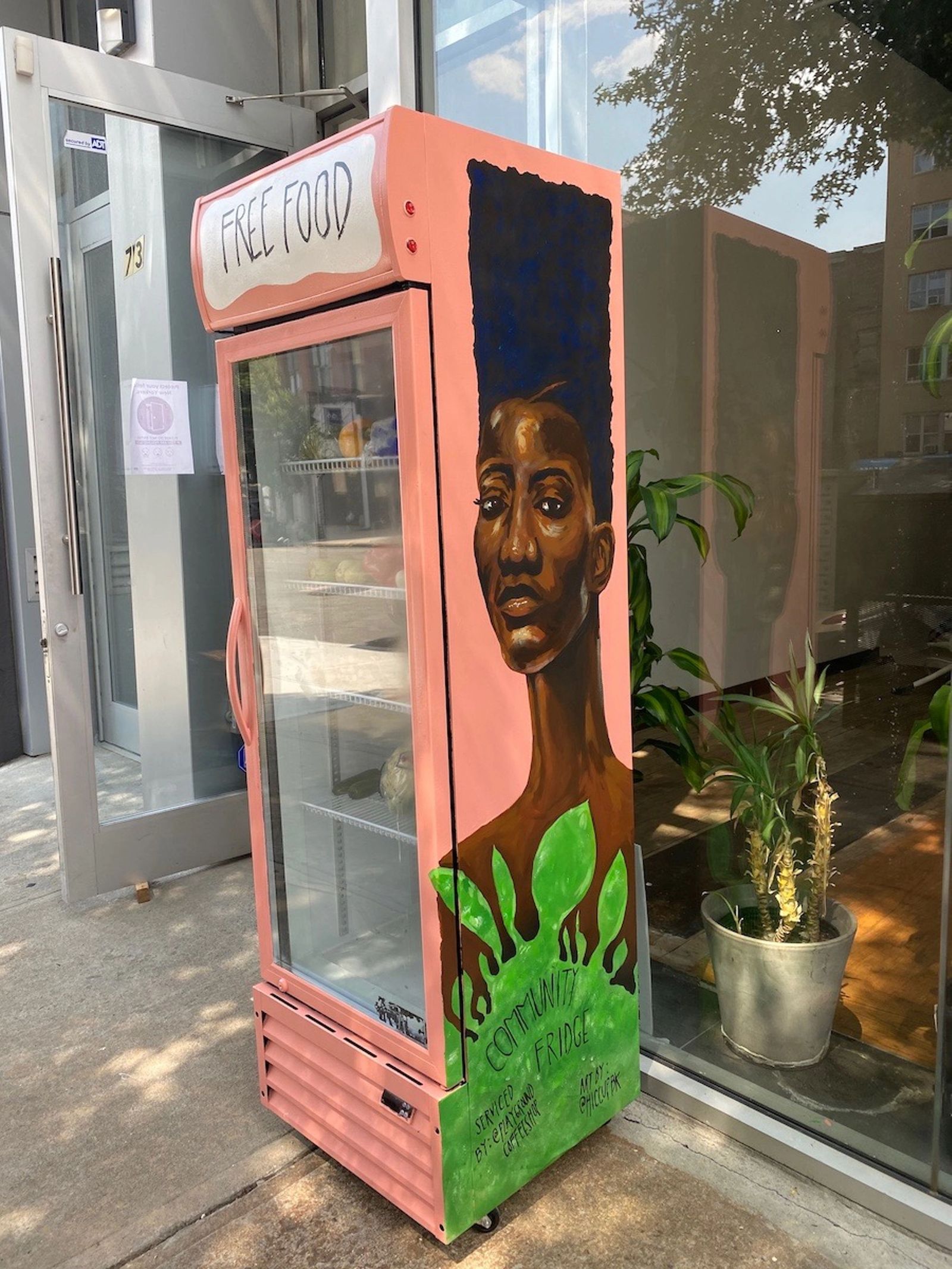 Coral-colored community fridge with striking Black woman painted on the side, outside of Beauty Strike