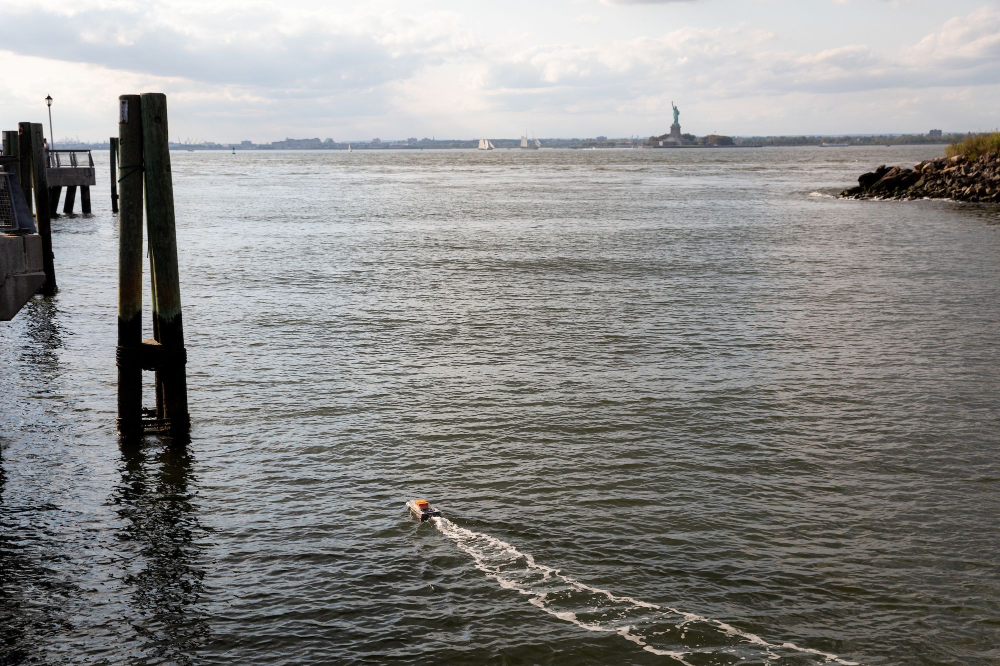 A small boat drives into the distance on the East River, with a stunning view of the Statue of Liberty in the distance behind it.