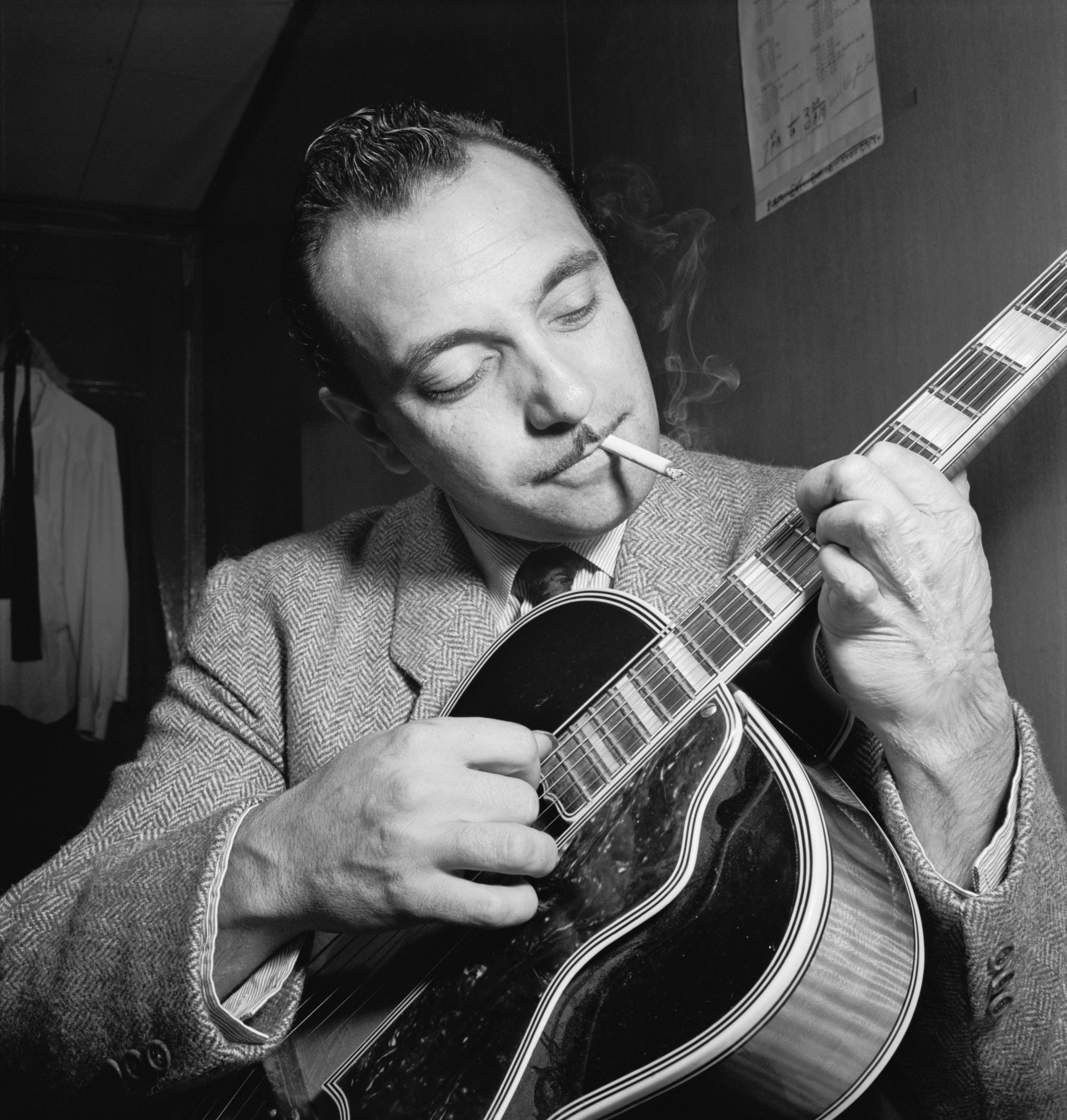 Django Reinhardt strums a guitar in a black and white photograph