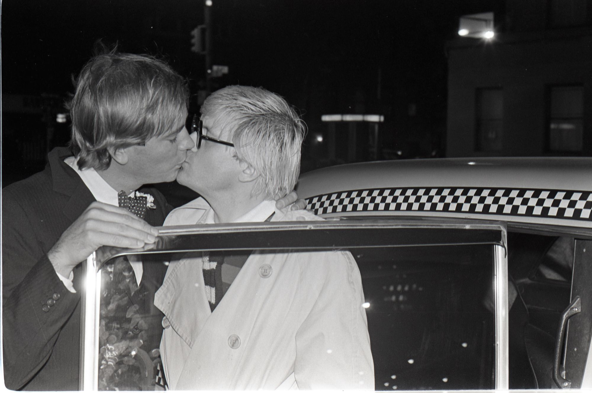 David Hockney shares kiss with man behind open taxi door.