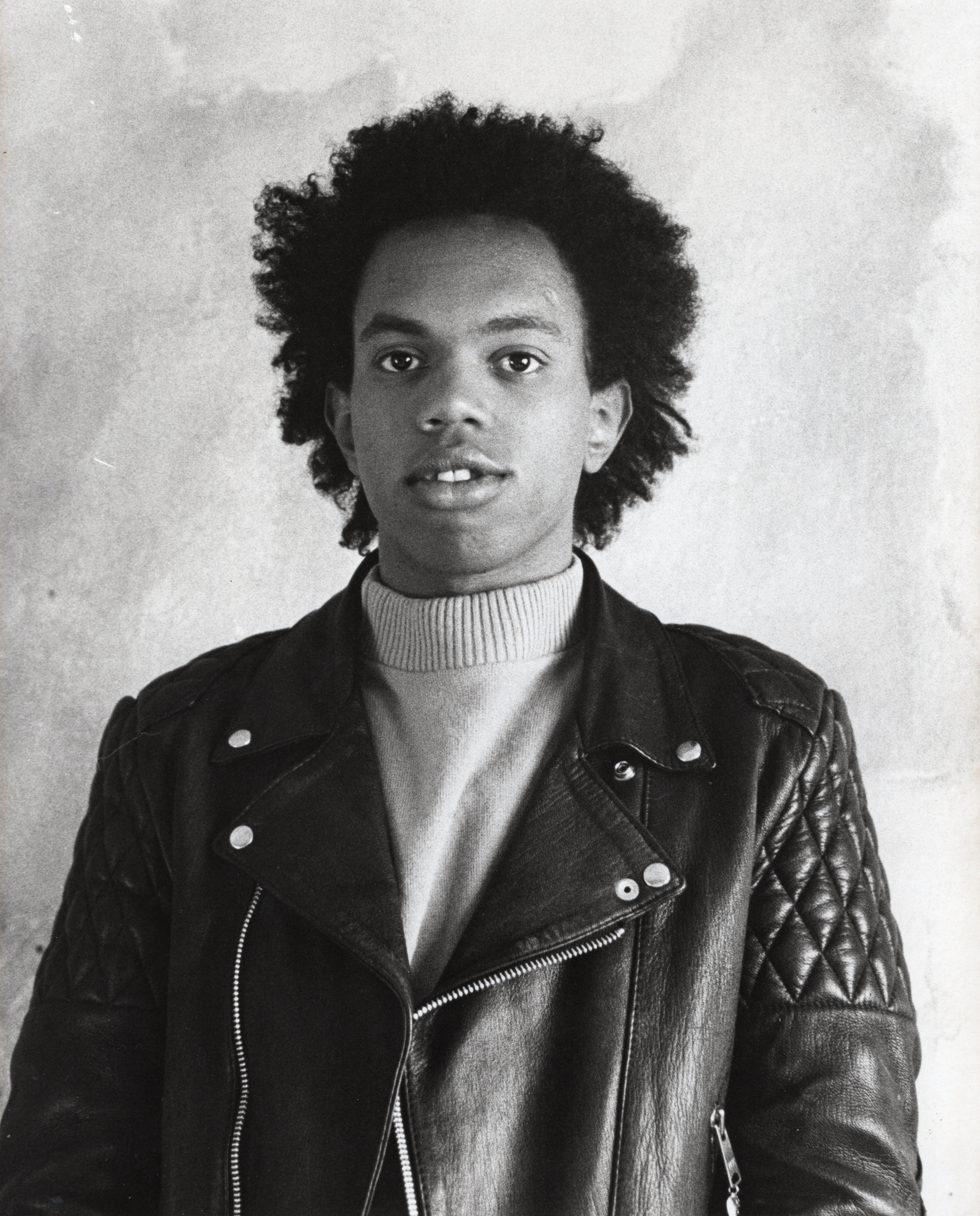 A black and white portrait of a person in a leather jacket and a turtle neck, making direct eye contact with the camera.  