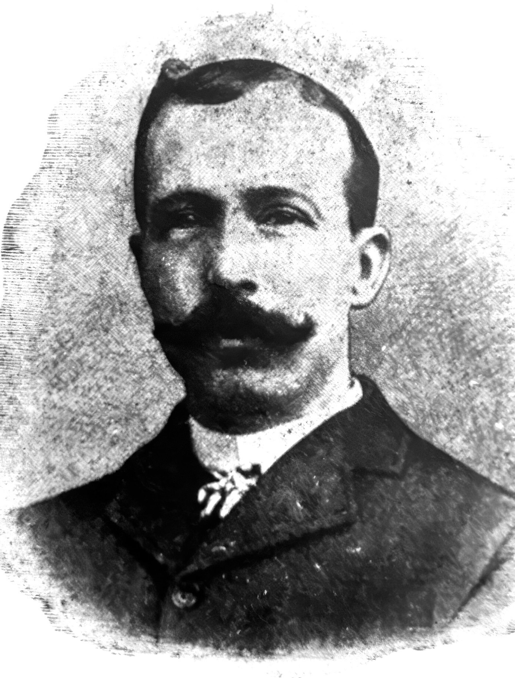 A black-and-white portrait of a young white man at the turn of the century, seen with a dark handlebar mustache.