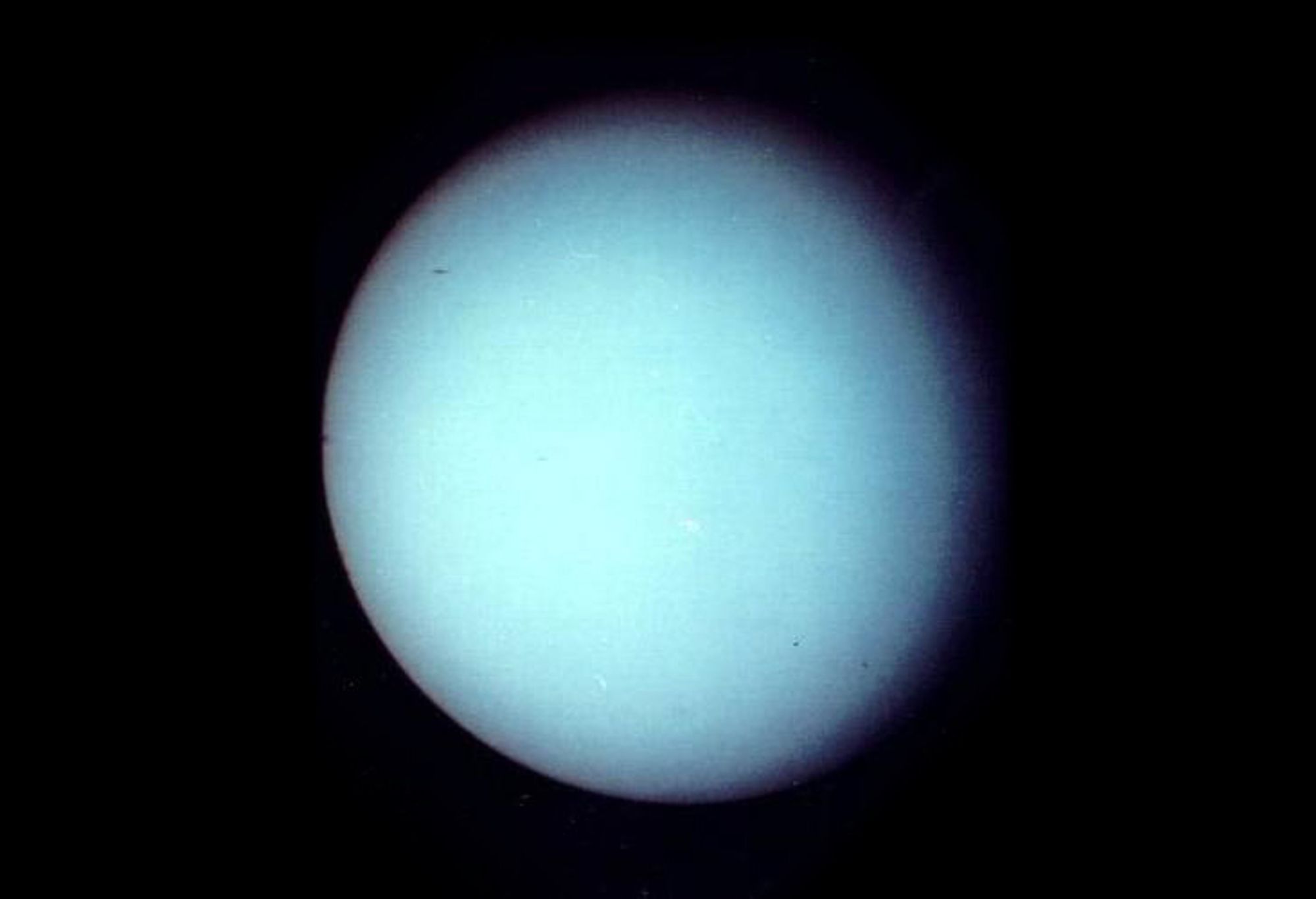 A grainy photograph of the light blue planet, Uranus.