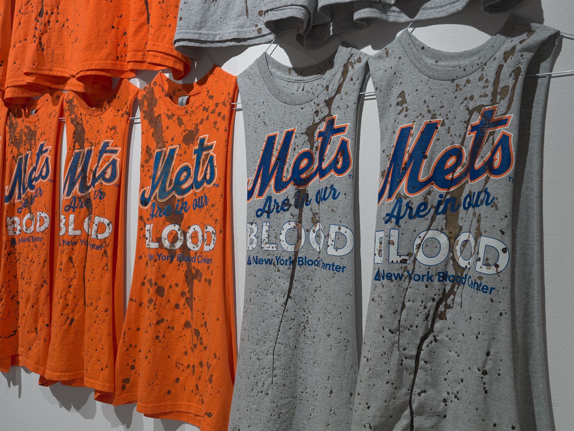 Row of orange and grey t-shirts with the sleeves cut that read "The Mets Are In Our Blood".