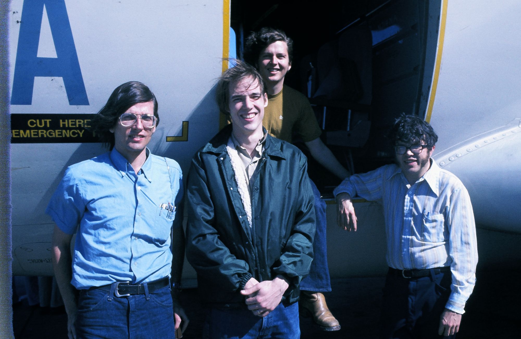 Four young astronomers smile for the camera in front of an airplane.