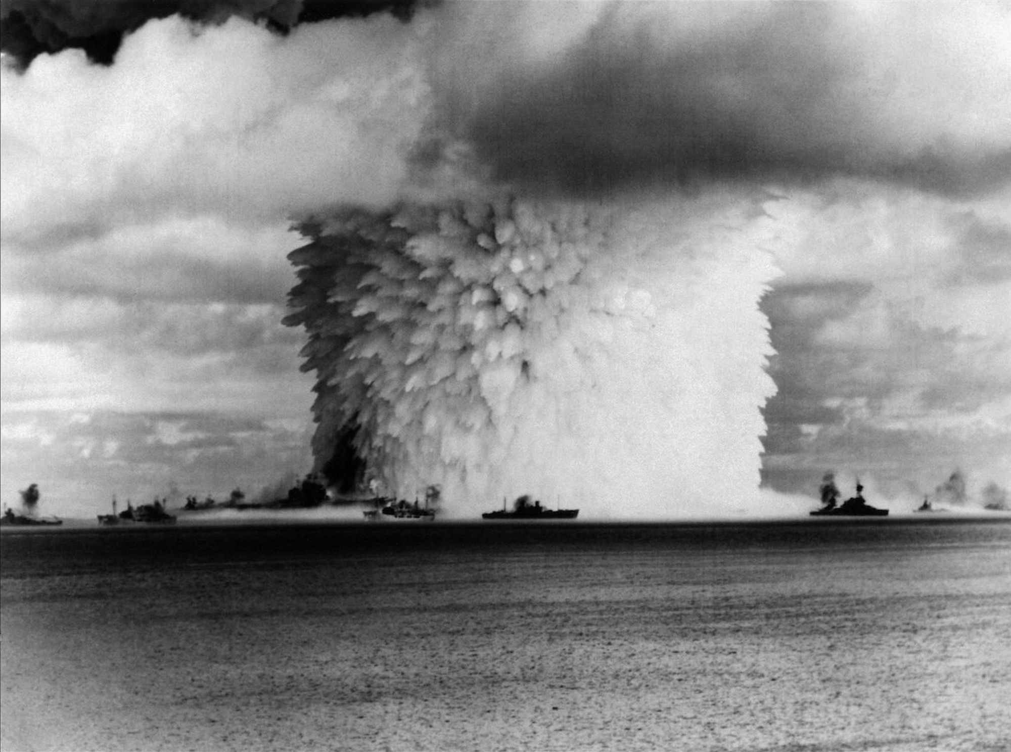 Crossroads Baker nuclear weapons test, 26 July 1946: view taken from Eneu island ten seconds after the weapon was fired. The aircraft carrier USS Saratoga (CV-3) is visible in the left foreground, being lifted out of the water. 