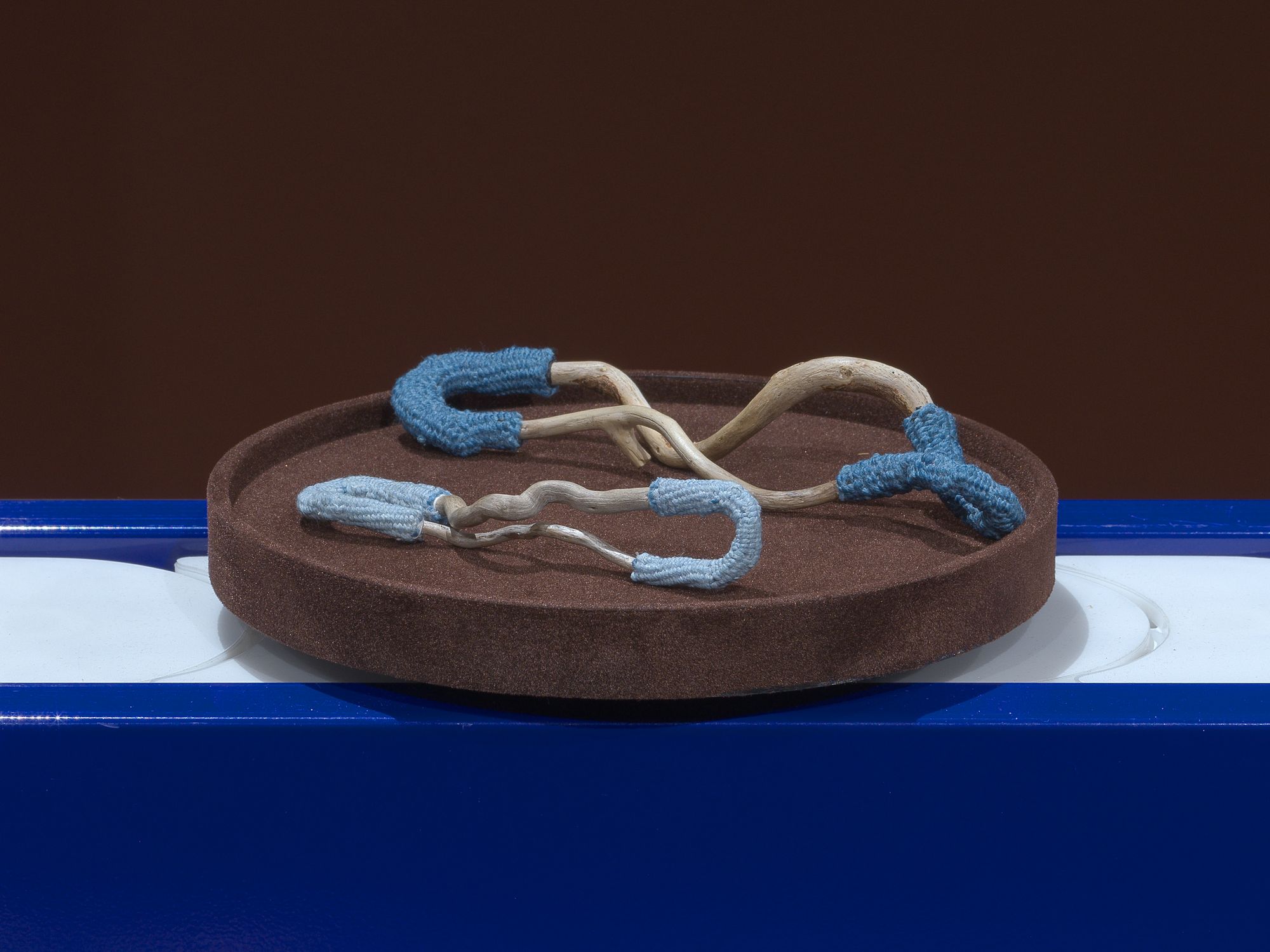 Two half-embroidered sticks in the shape of wishbones, resting on brown plates which move along a blue conveyor belt.