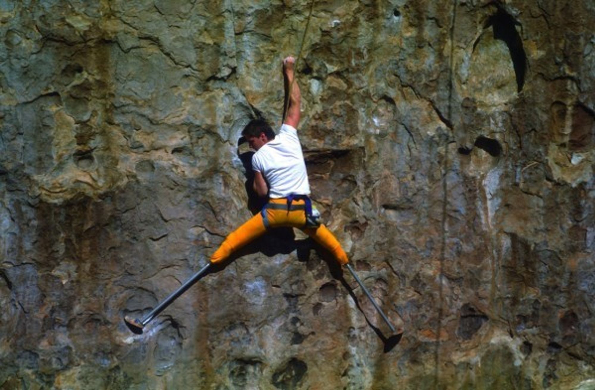 Hugh Herr climbing a rock face with long prosthetic legs.