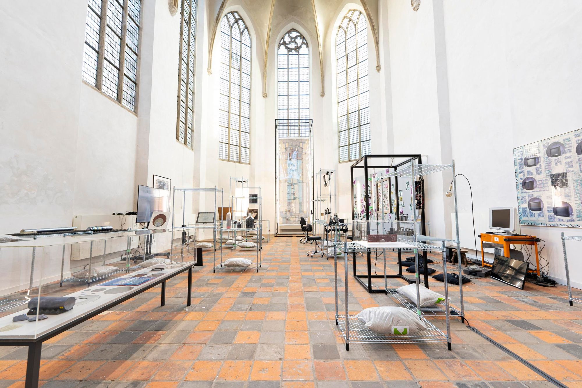 A photograph of an exhibition taking place in a church-like space, with large lancet windows beaming light into the room.