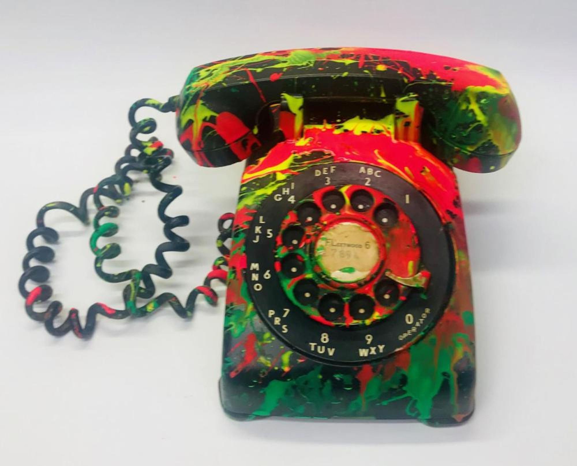 Black rotary phone covered with colorful paint splatters. 