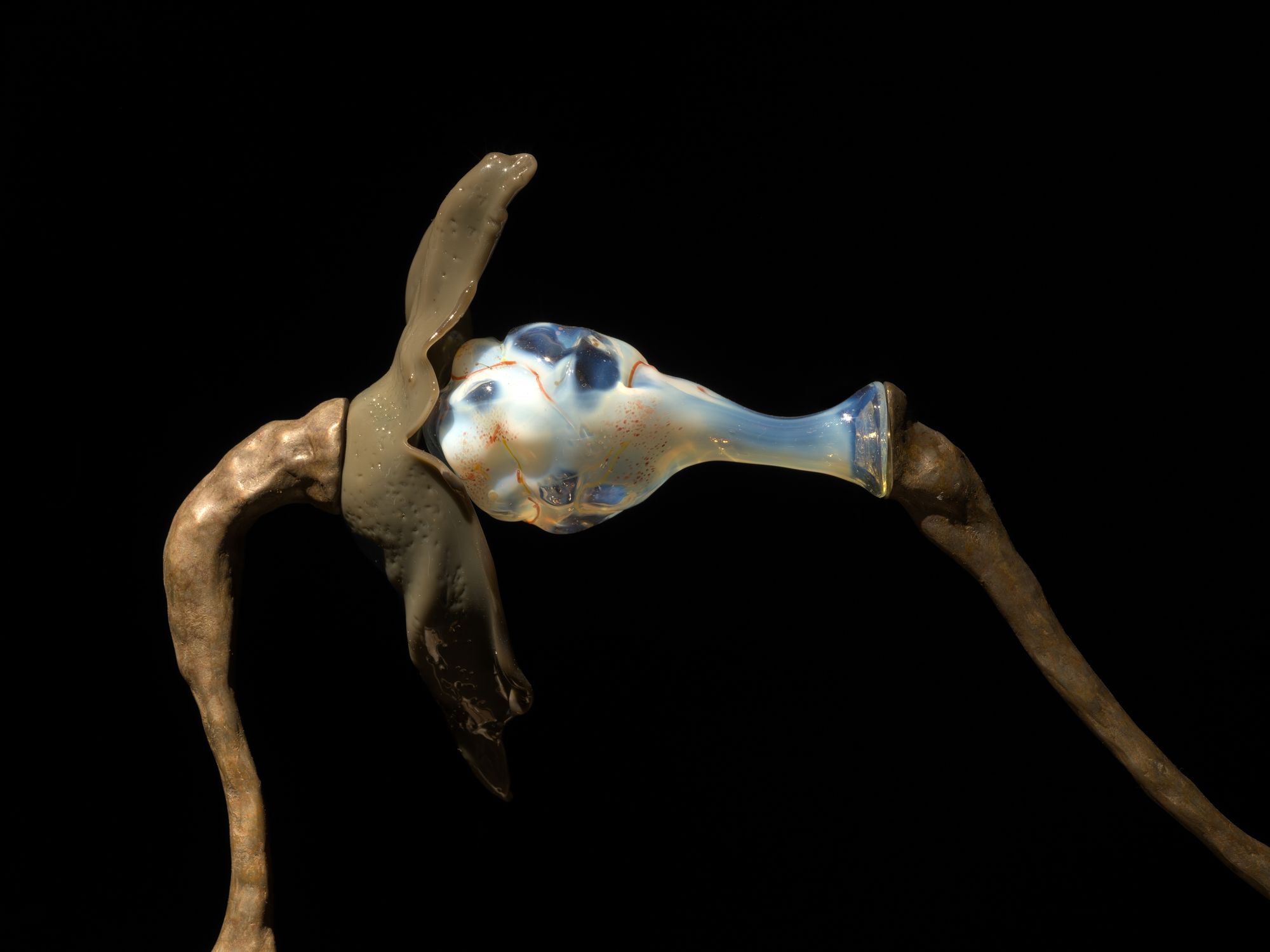 A close-up shot of a sculpture wherein a clear glass bud presses into a metal flower