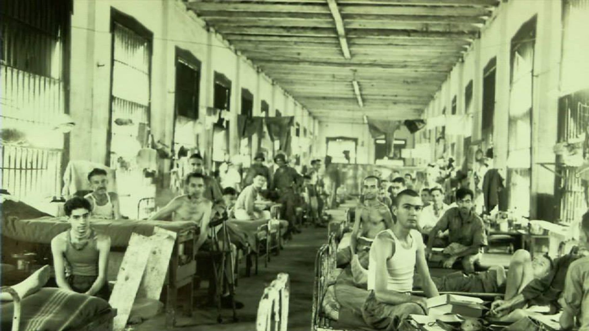 A sepia-toned image of soldiers in a prison camp. All the soldiers are facing and staring straight at the camera, with blank expressions.