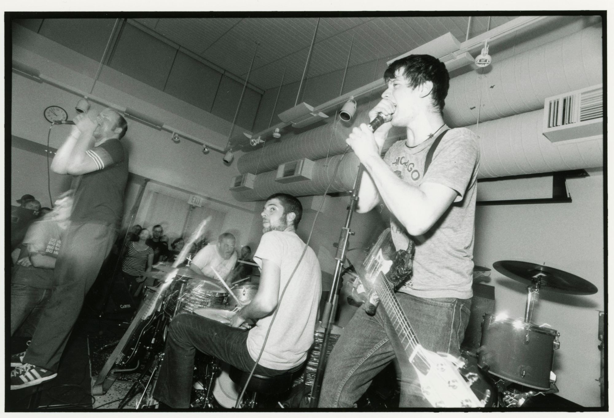 A black and white film photograph of a punk band playing a show.