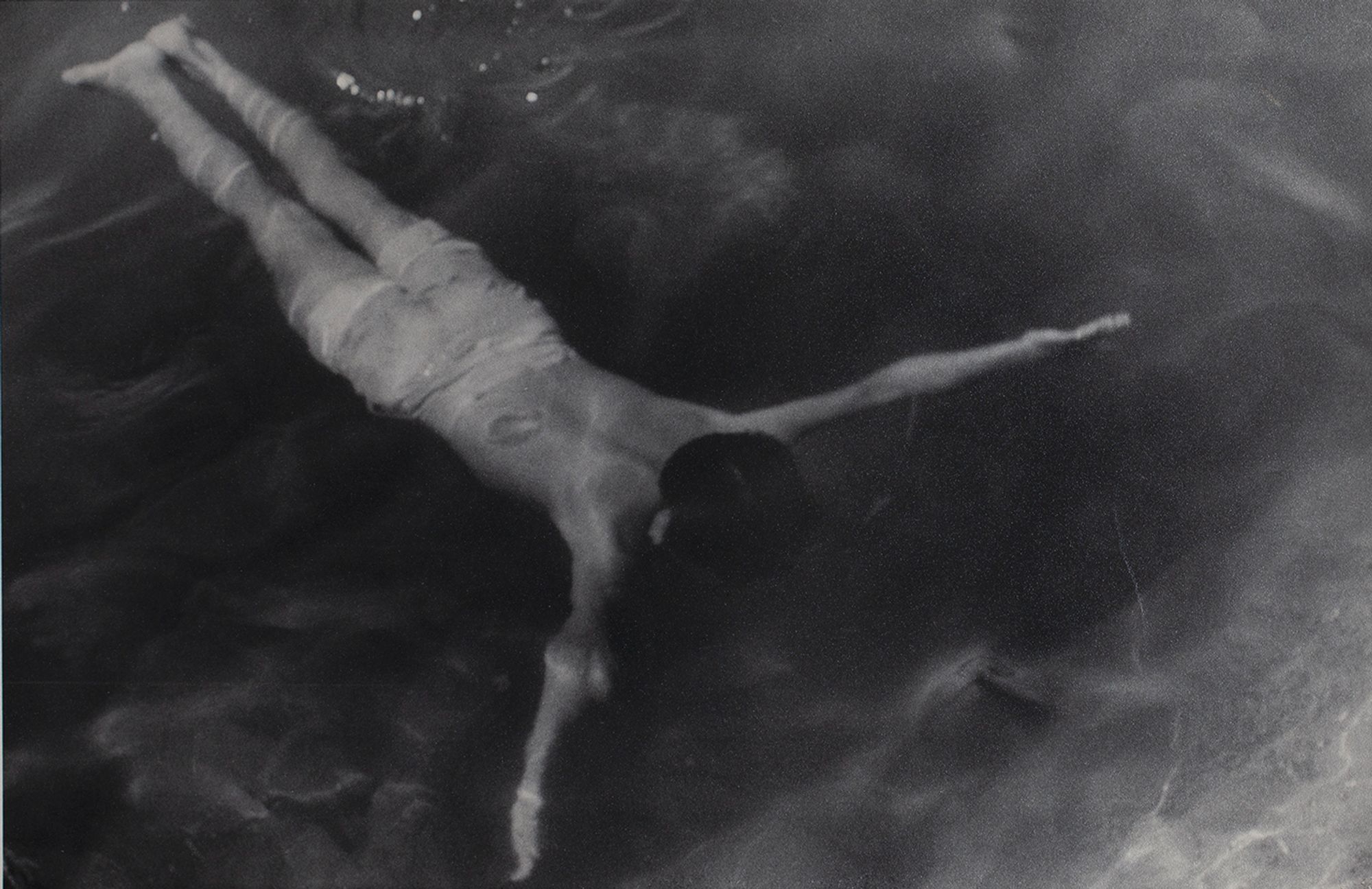 A black-and-white photograph of a swimmer underwater. The swimmer's body is shaped in a Y-formation as he extends his arms symmetrically straight out to his side