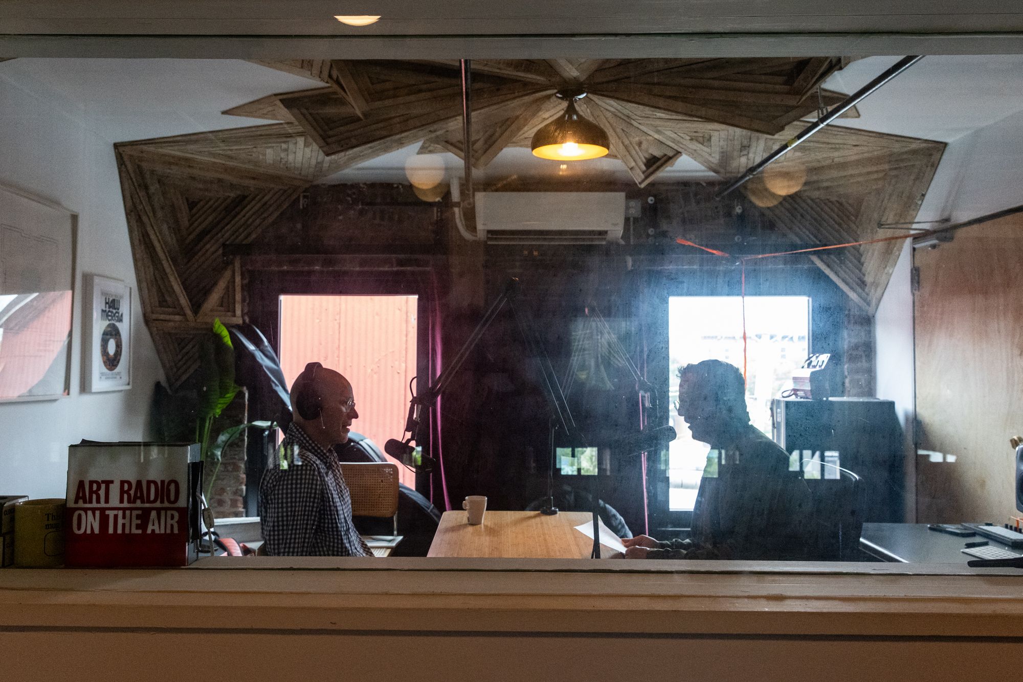 Two men speak into microphones inside a radio booth