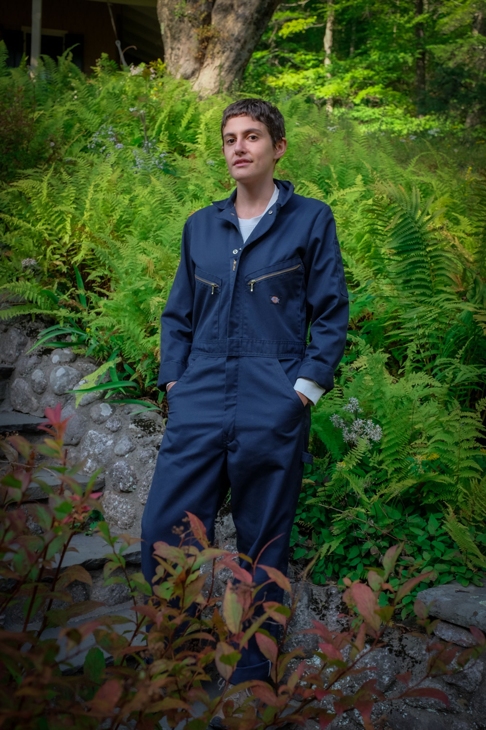 A person wearing a navy dickies jumpsuit against a lush landscape of greenery.
