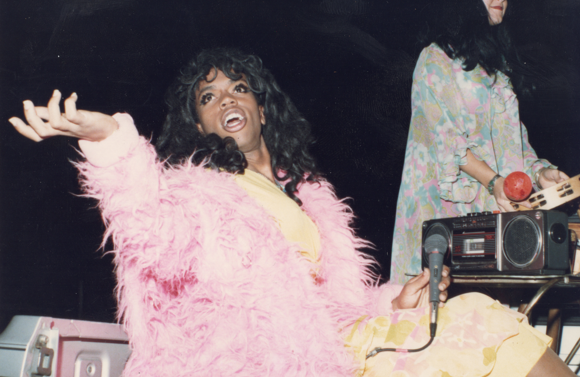 Sean DeLear, performing in drag, wearing a pastel pink fur coat and a long wig. 