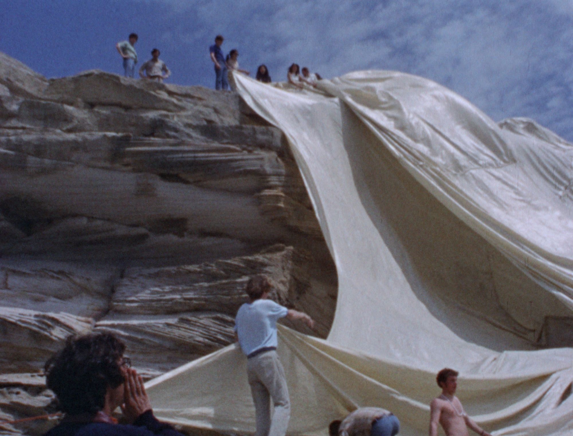 A group of people wrap a cliff front with white fabric.
