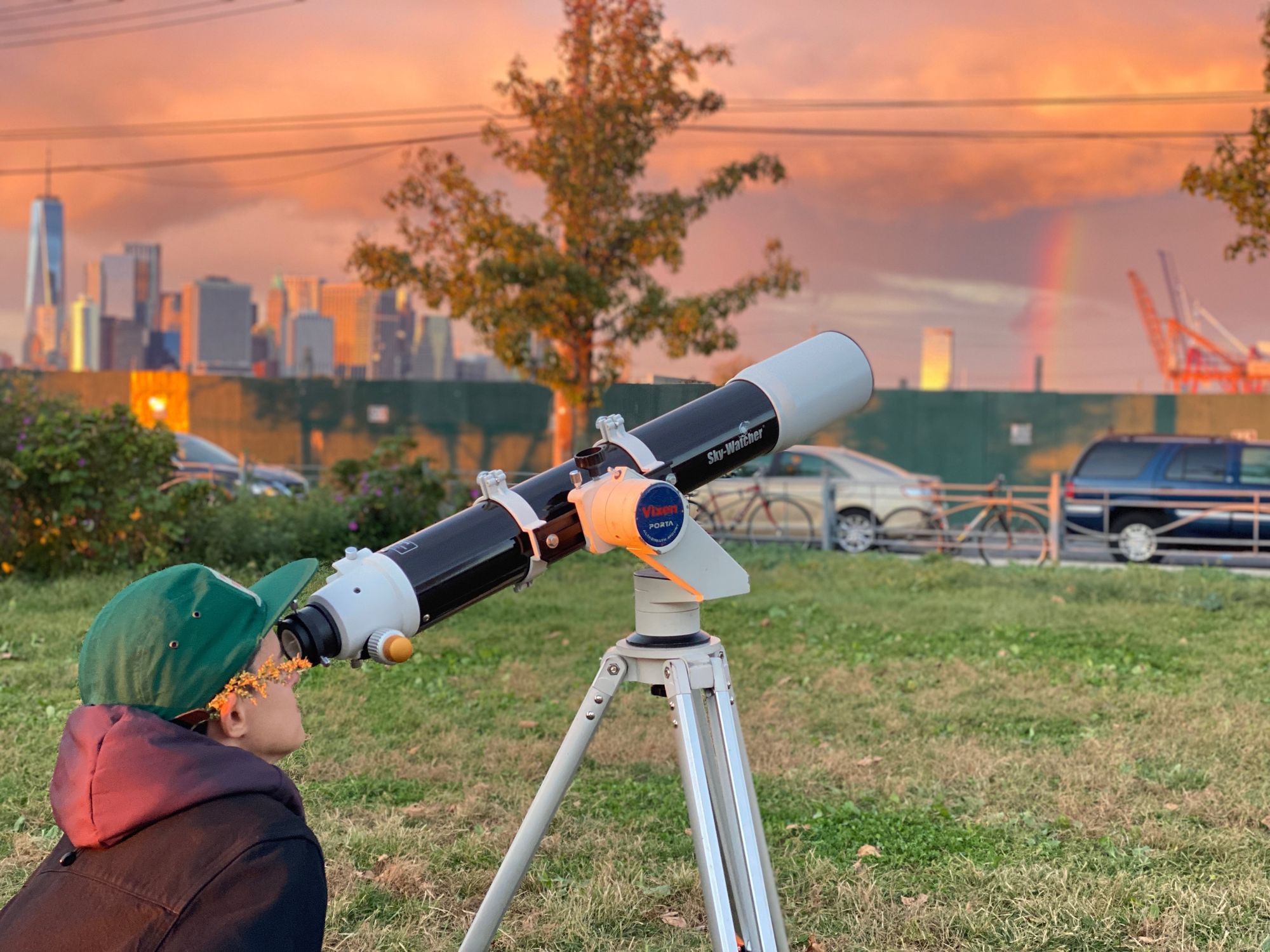 A person peering into a telescope, with NYC in the background