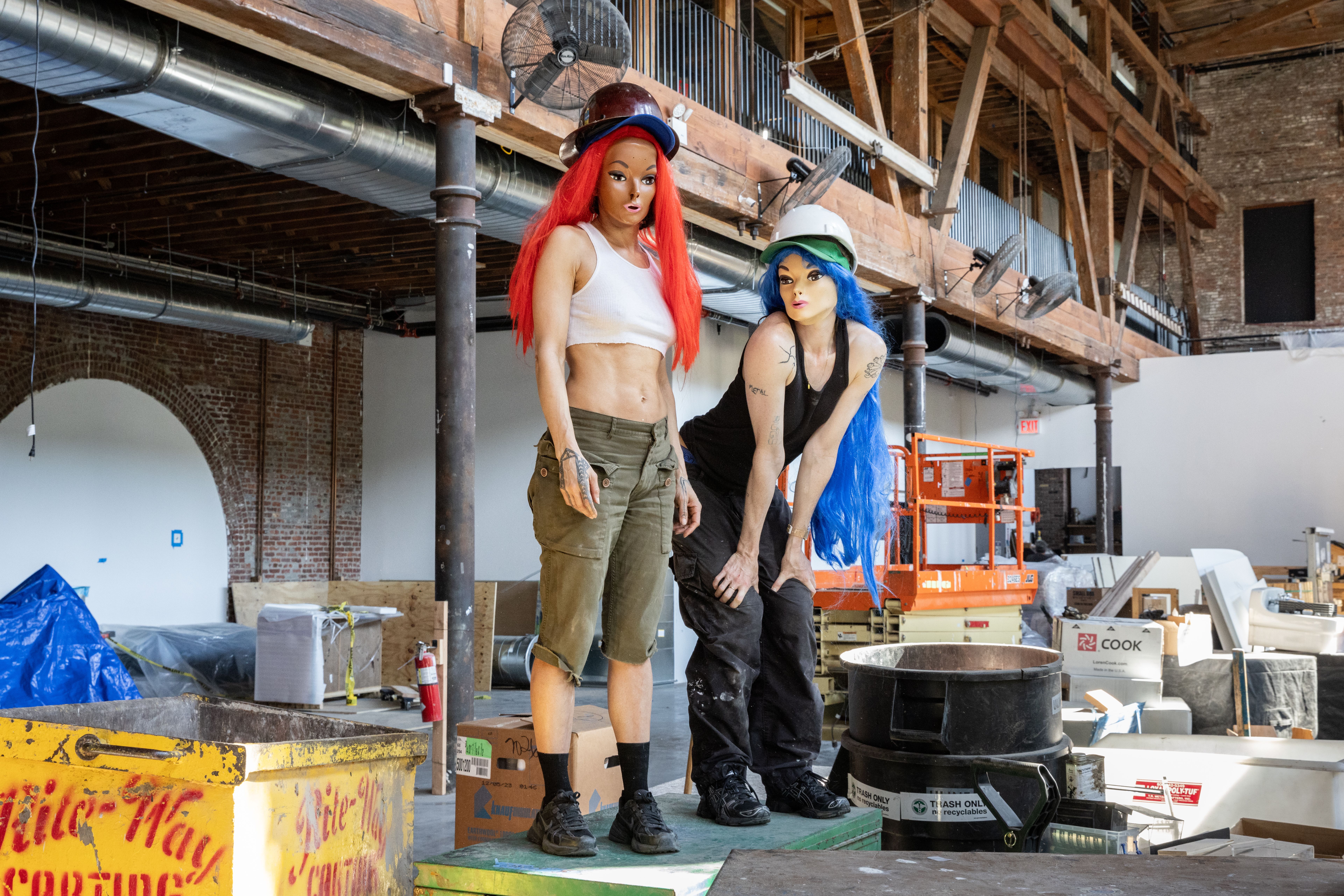 A woman balances amidst a construction site in black stilettos and red socks, her face covered with a mask a couple shades darker than her skintone.