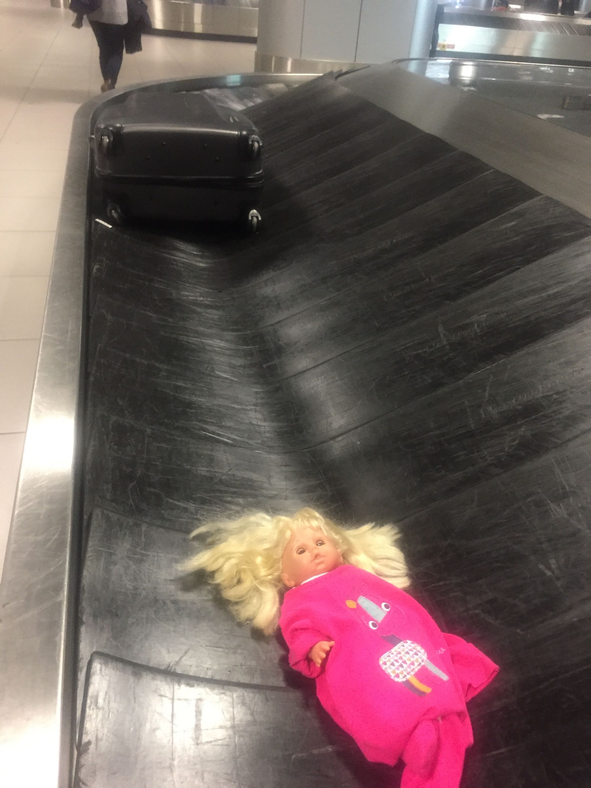 Photo of a doll on an airport baggage conveyor belt.
