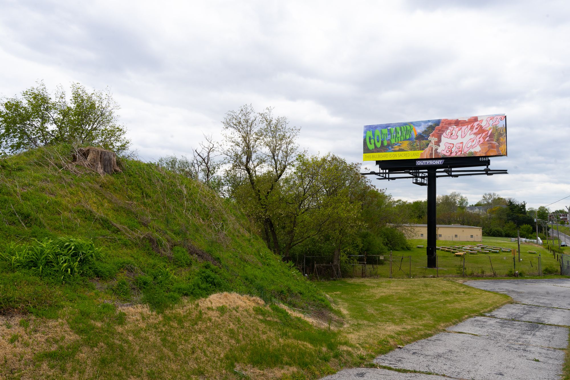A billboard on a grassy hill with cartoonish lettering that reads: "This billboard is on sacred land."