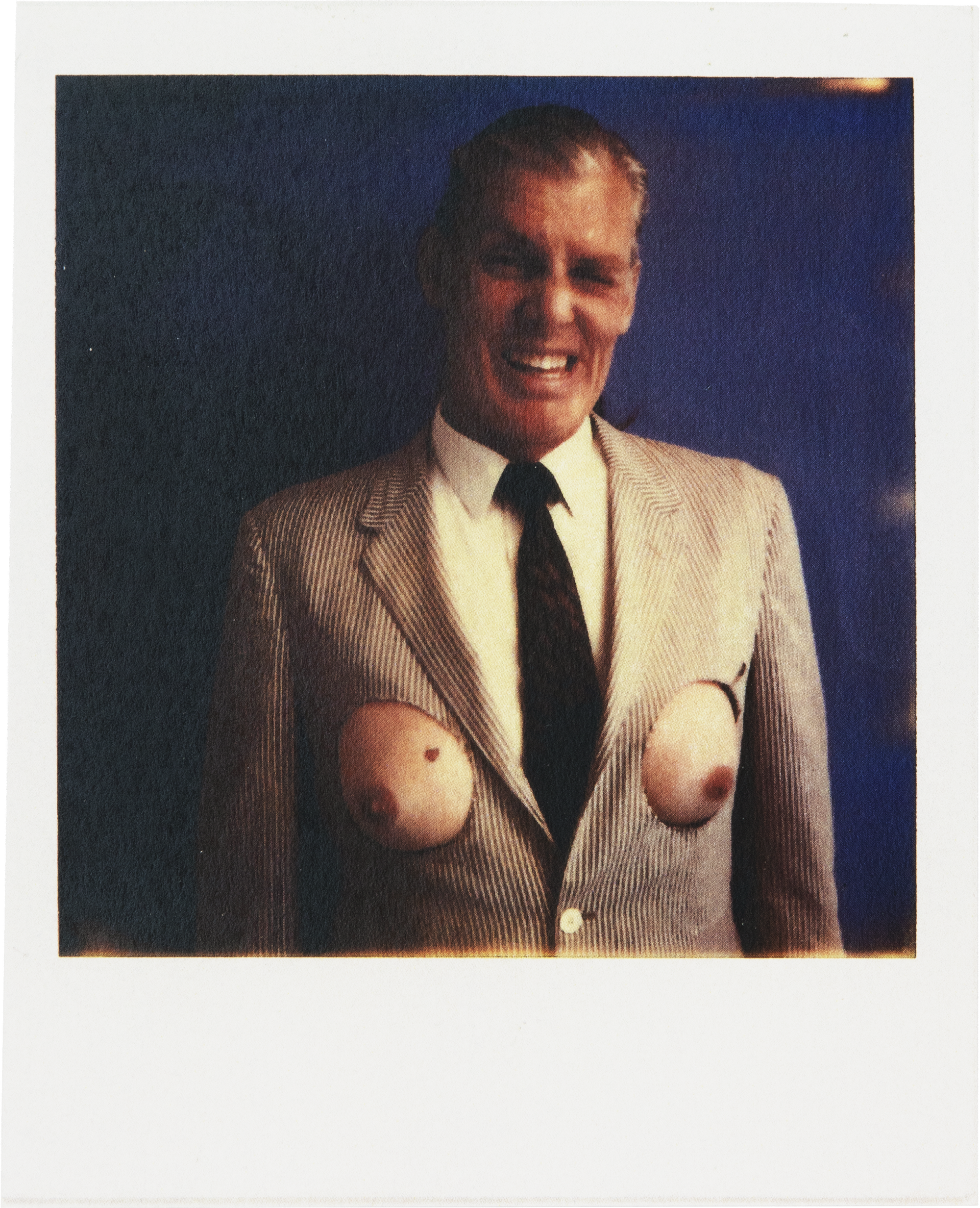 A masculine figure wears a suit where holes are cut symmetrically to reveal full breasts.
