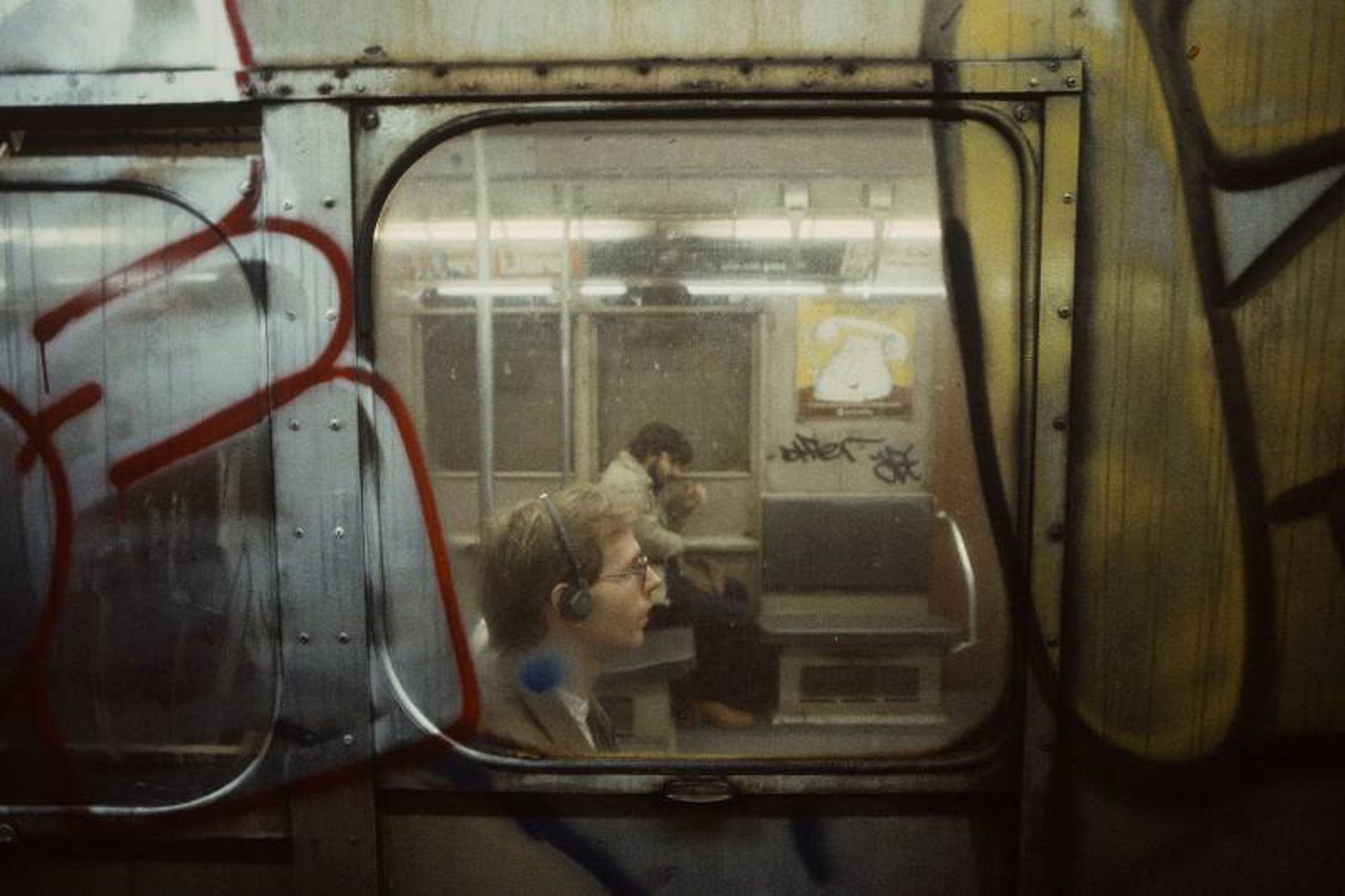 Photo from the subway of a person in another subway car listening to a walkman.