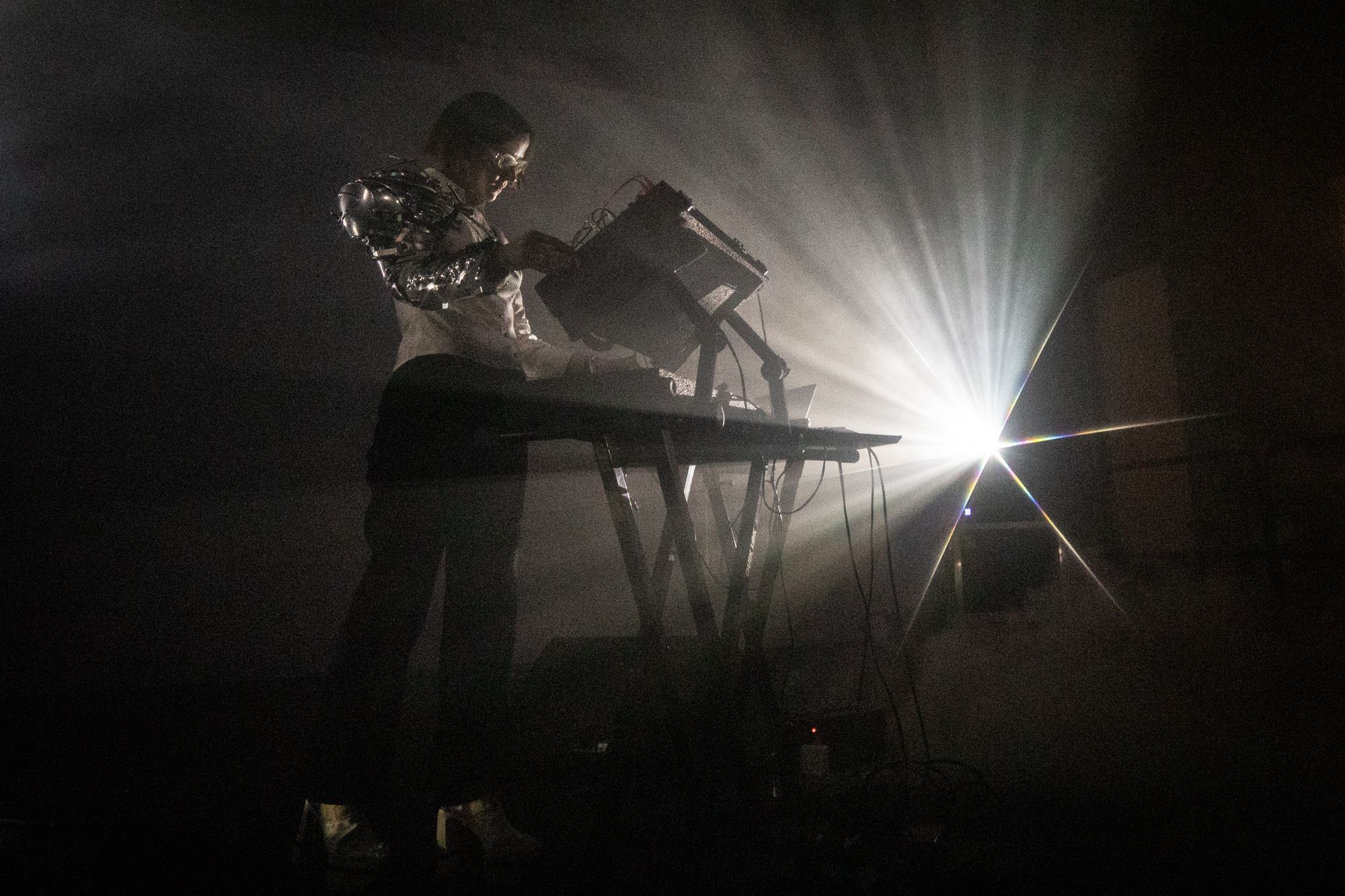 A woman stands in a dark room behind a table of keyboards and instruments.