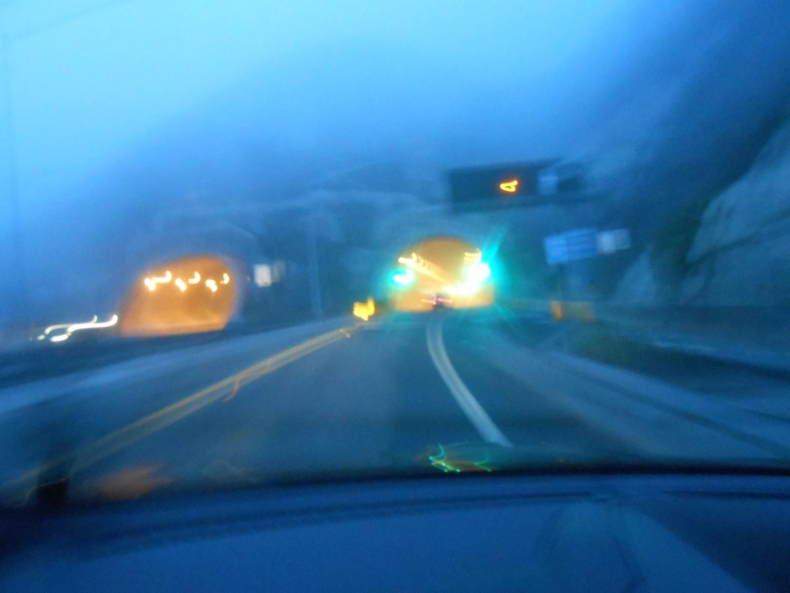 A blurry, blue-tinted photograph from within a car overlooking a freeway and approaching a yellow-lit tunnel.