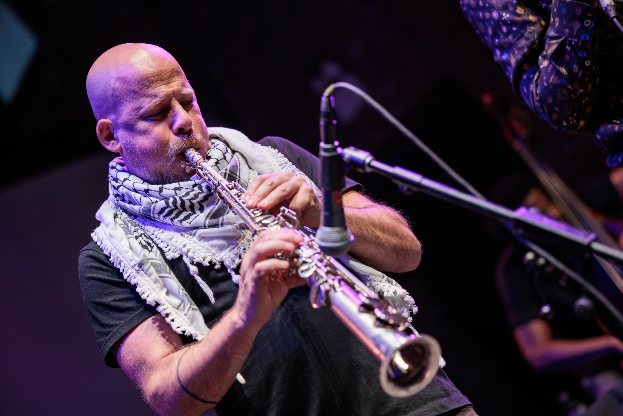 A figure wearing a keffiyeh blows into his saxophone.