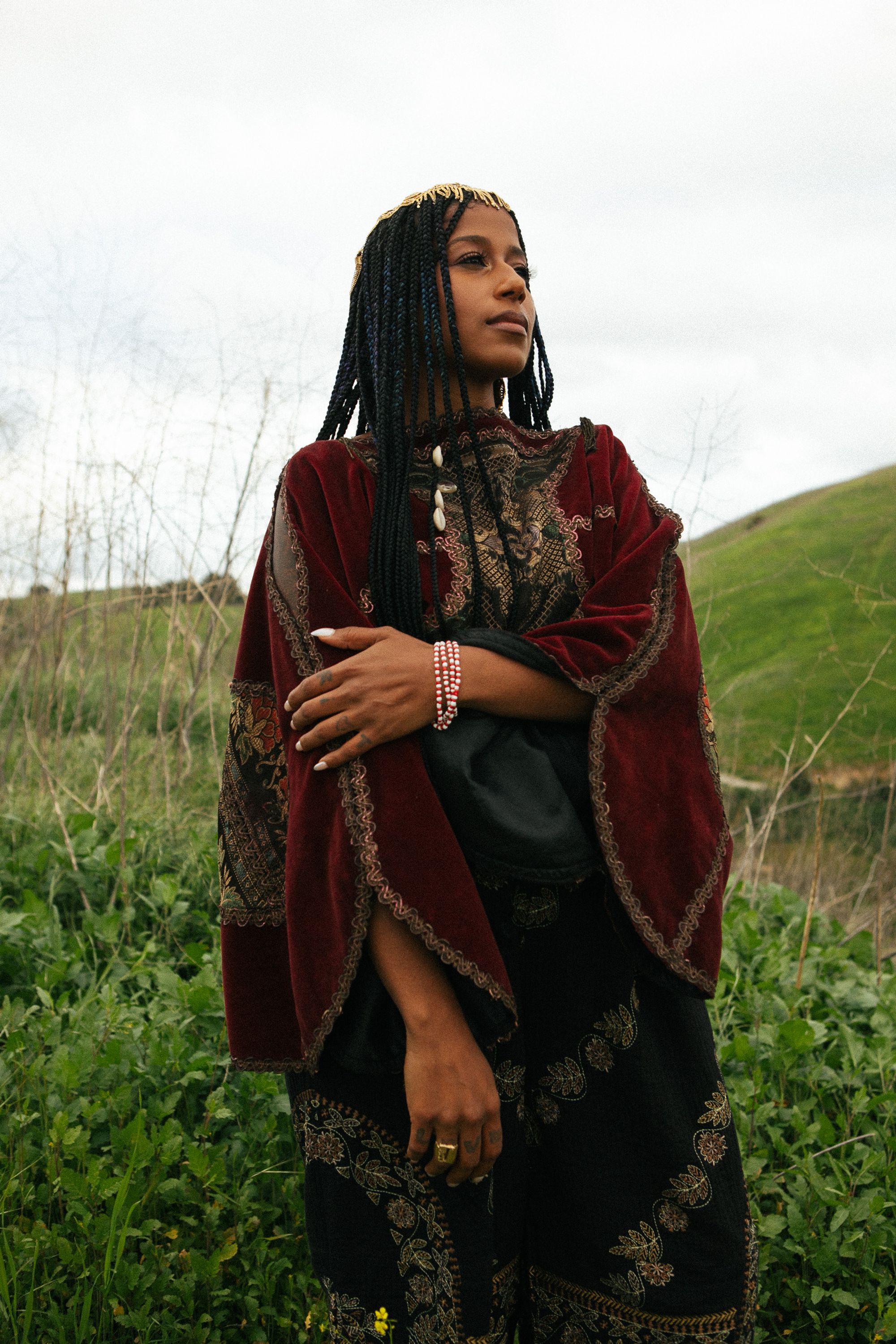 aja clothed in dark red robes in front of a lush green hill