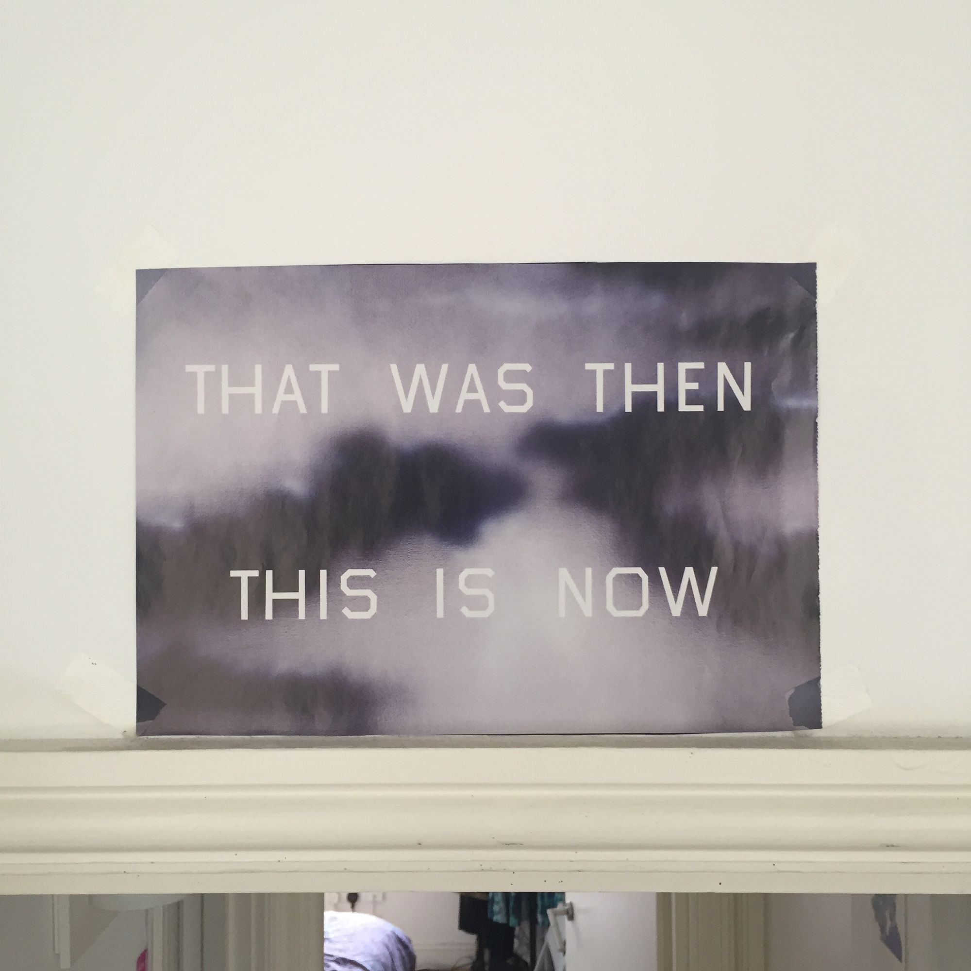 A photoraph of Ed Ruscha's gray-toned painting with the words "That Was Then This Is Now II" pasted above a doorway.