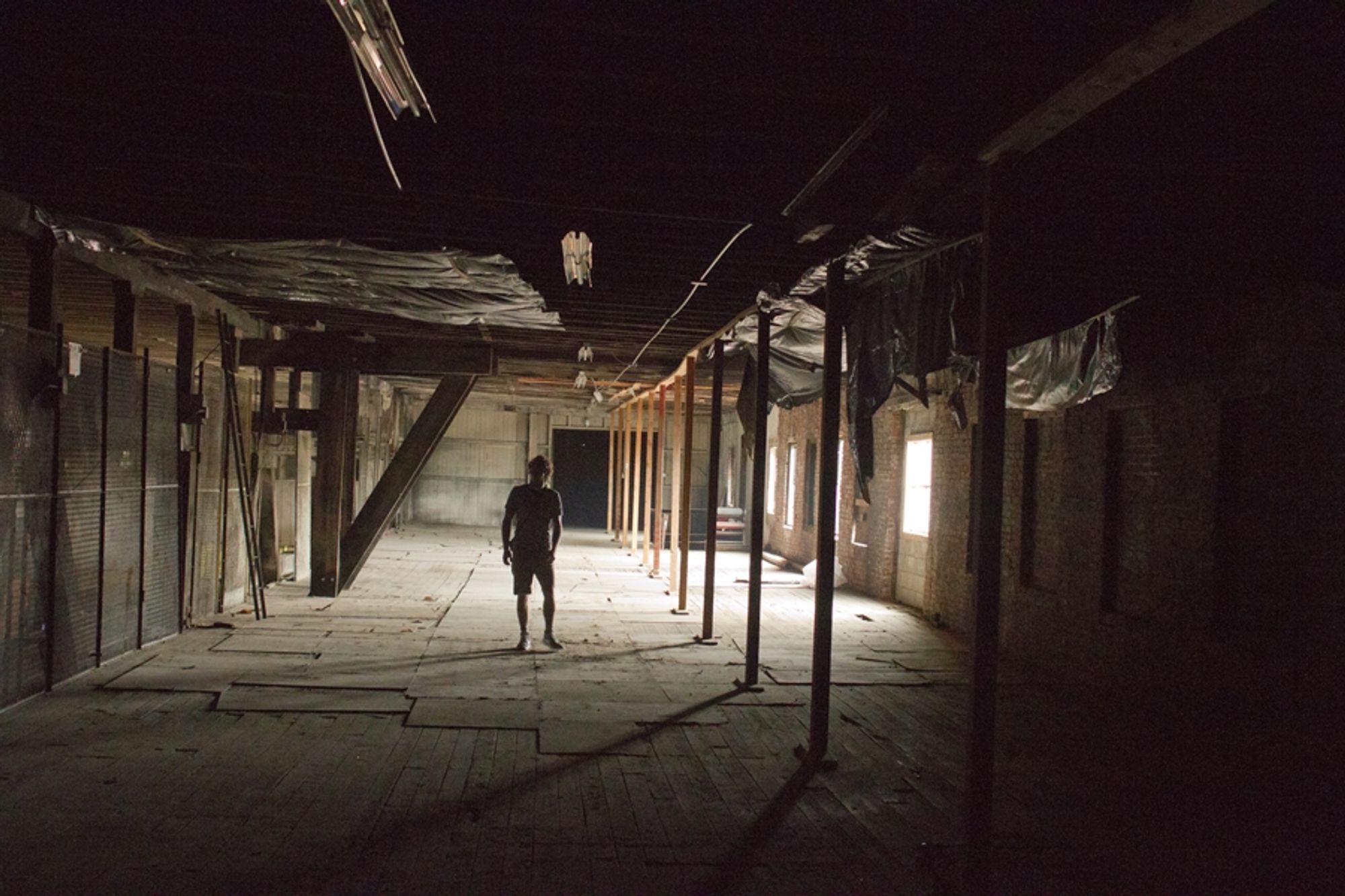 A figure stands in an abandoned industrial building, backlit by the window towards the back of the small room.