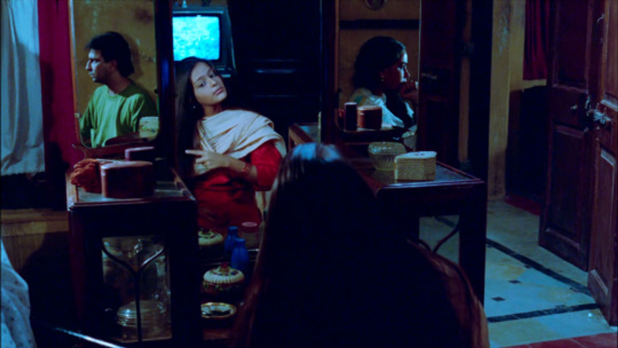 Three people in a kitchen facing a mirror. The middle person is most visible and is looking at herself in the reflection