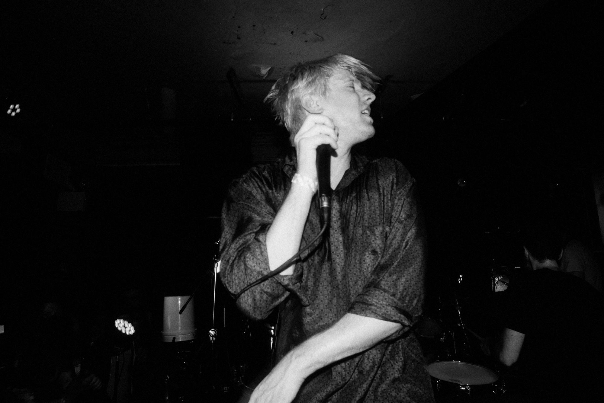 A black and white image of a man with bleached hair, clutching a microphone and shaking his head.
