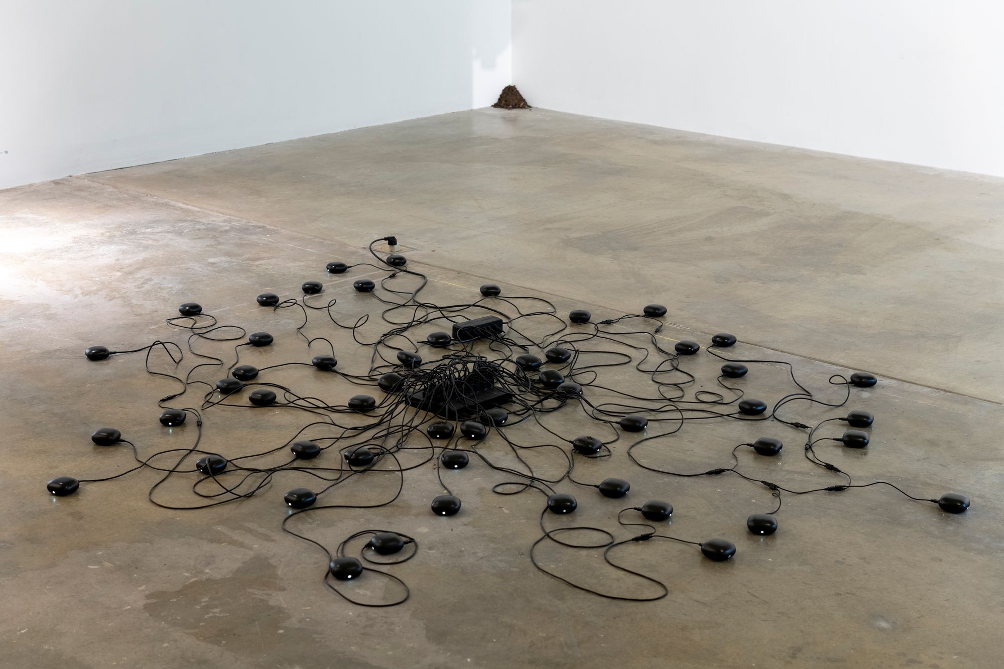 A tangled web of black devices and their cords expanding from the center of the floor in an exhibition space.