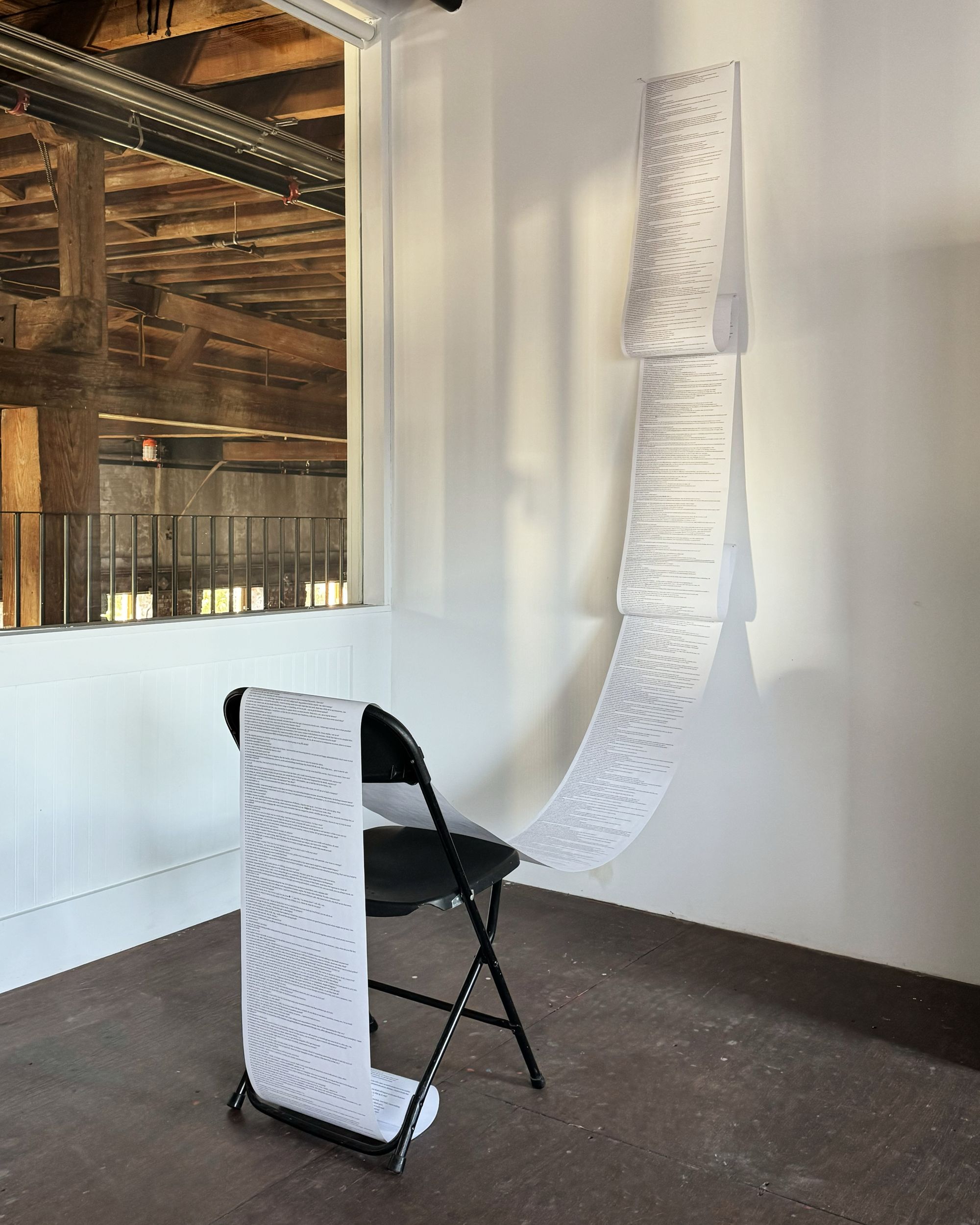 A scroll extends from a white wall where it's been attached, spilling across a folding chair. 