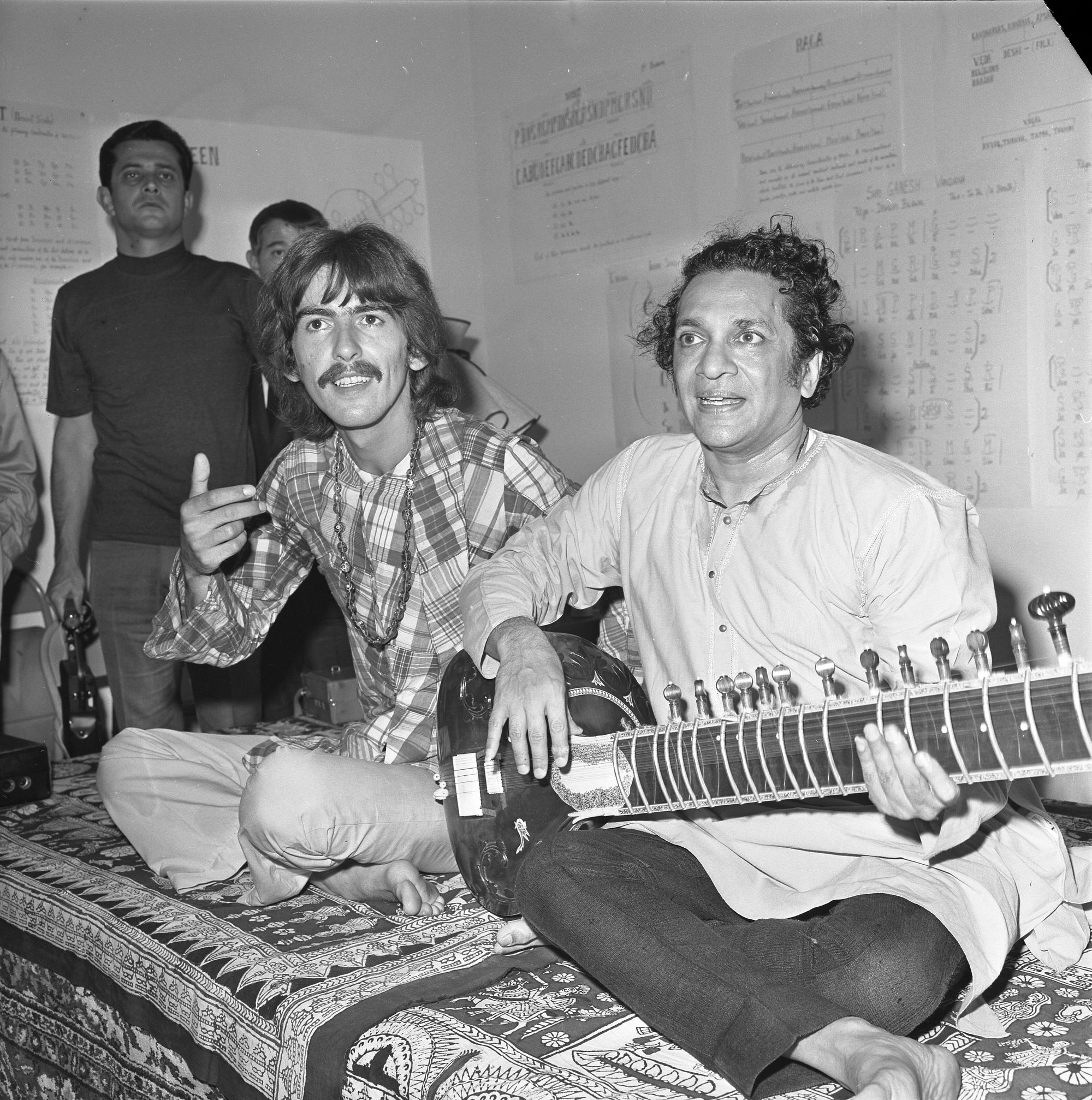 George Harrison sits next to Ravi Shankar, holding a sitar