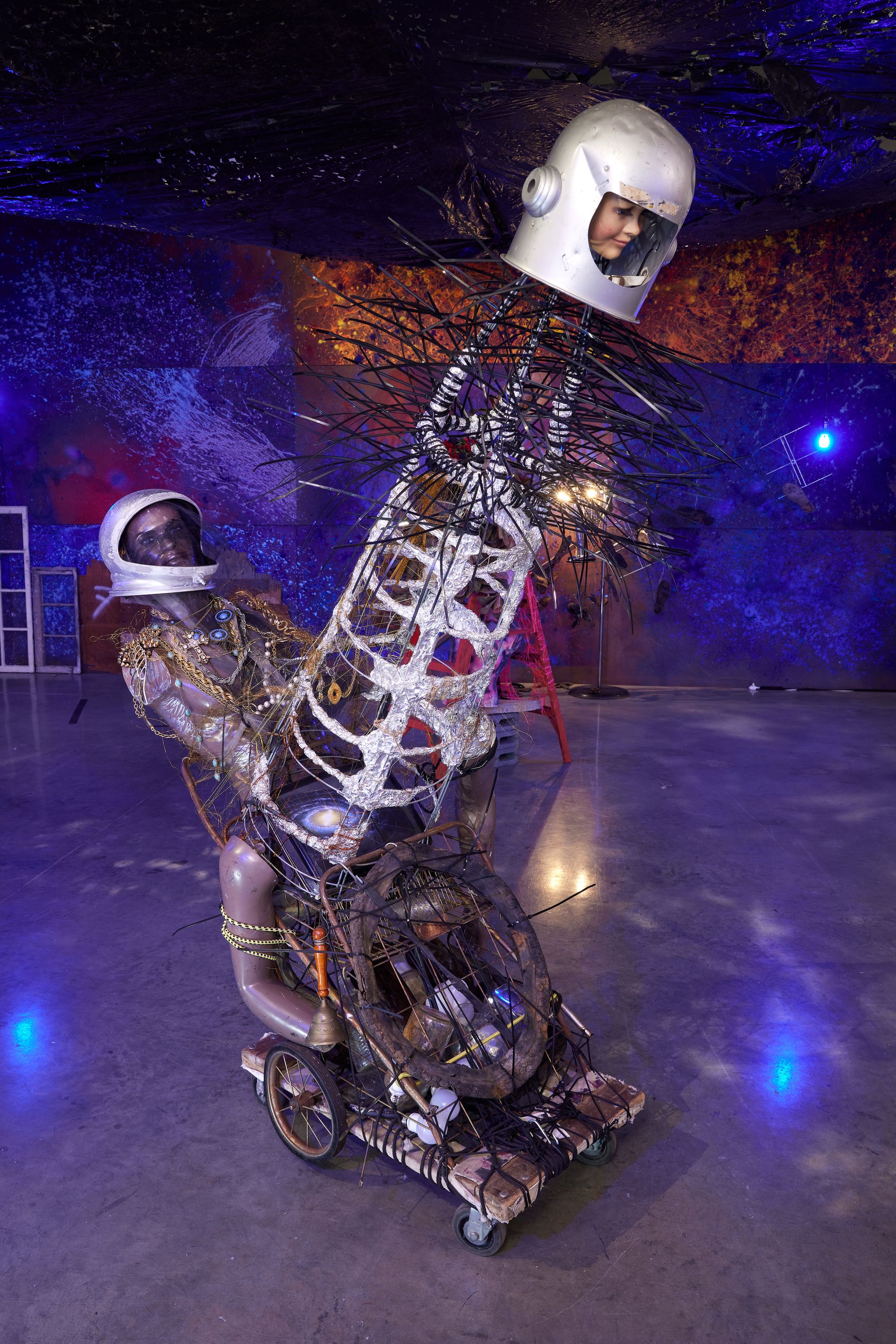 A dinosaur-looking creature assembled from mixed metals and materials, with a mannequins head on top wearing an astronaut's helmet.  