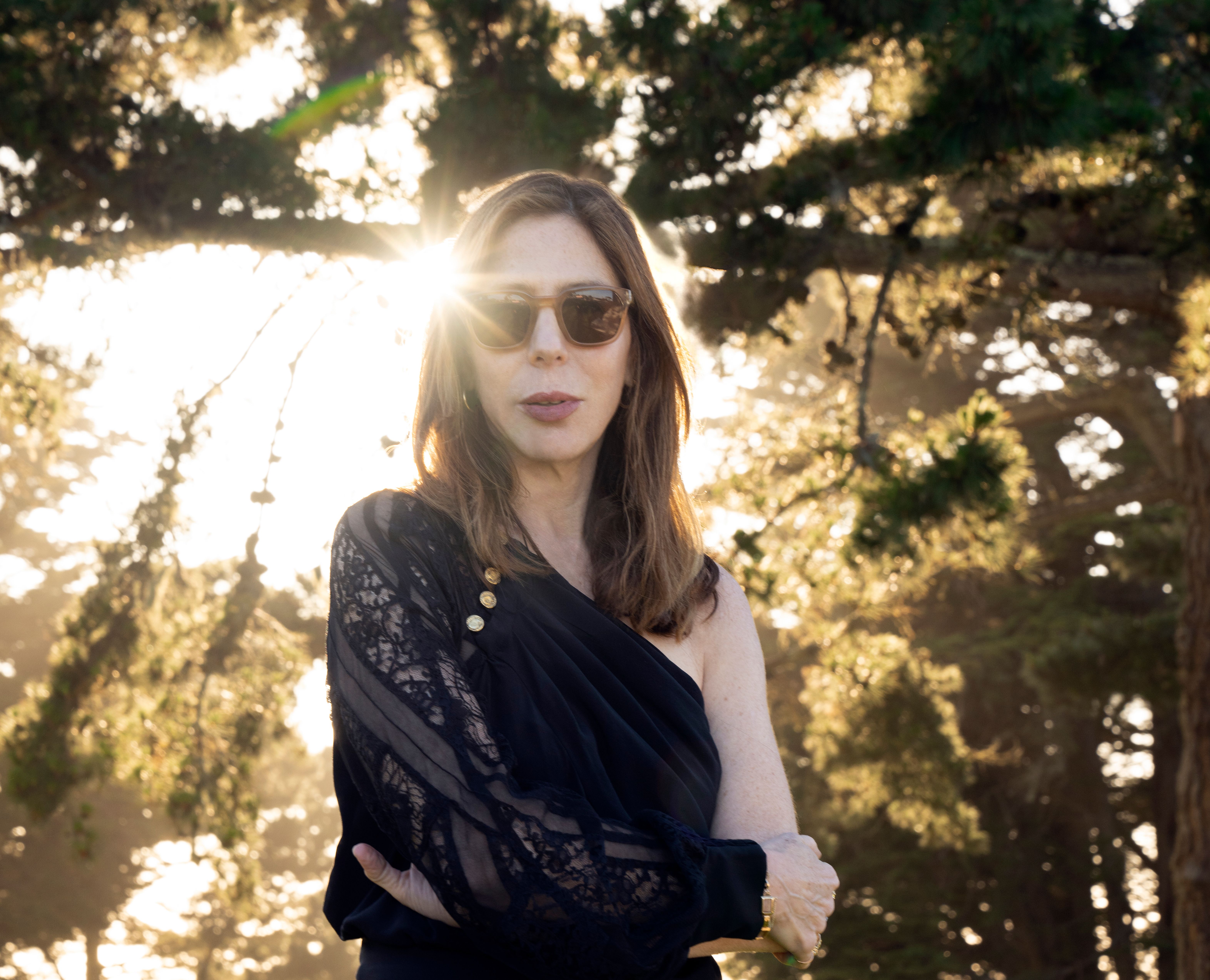 Photo of Rachel Kushner backlit by the sun and surrounded by trees