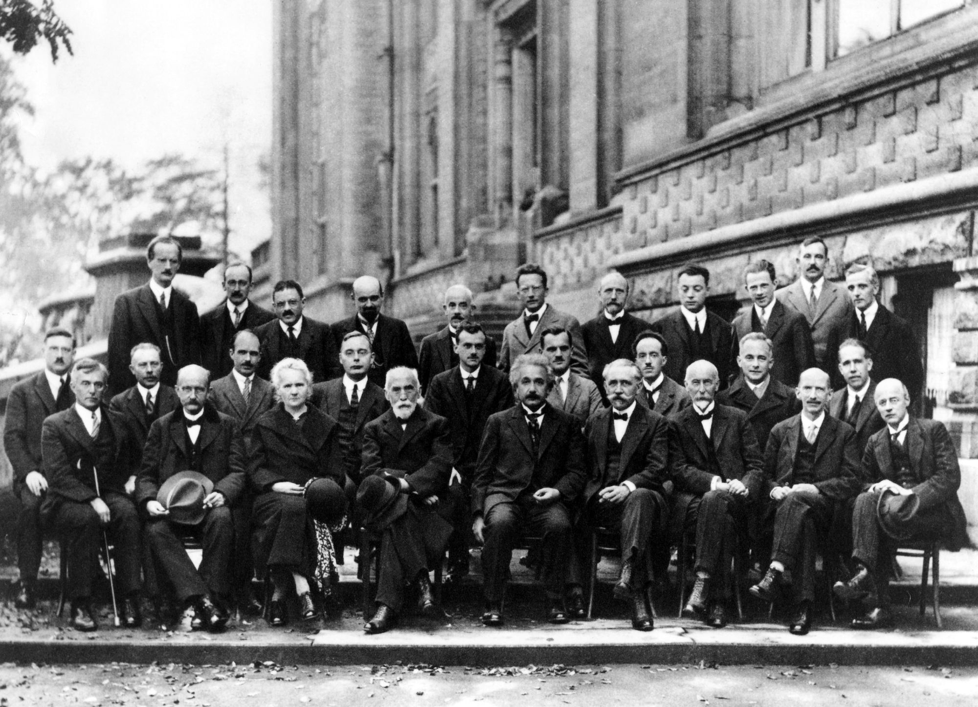A black-and-white posed photograph of scientists at a conference, including Einstein, Planck, Schrödinger, and Heisenberg. 