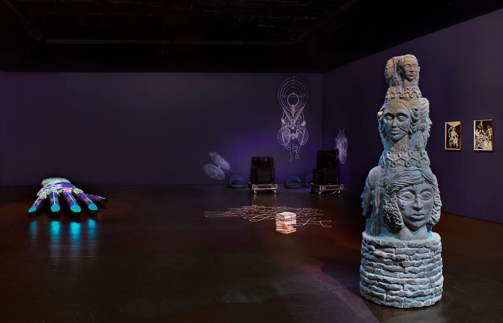 A wide shot of the exhibition "Her garden, a mirror," with a column of stone-like faces in the foreground.