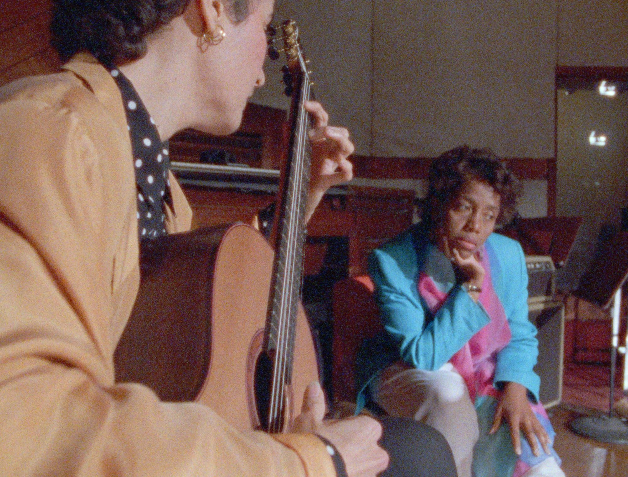 A man plays guiitar while a woman looks on mournfully.