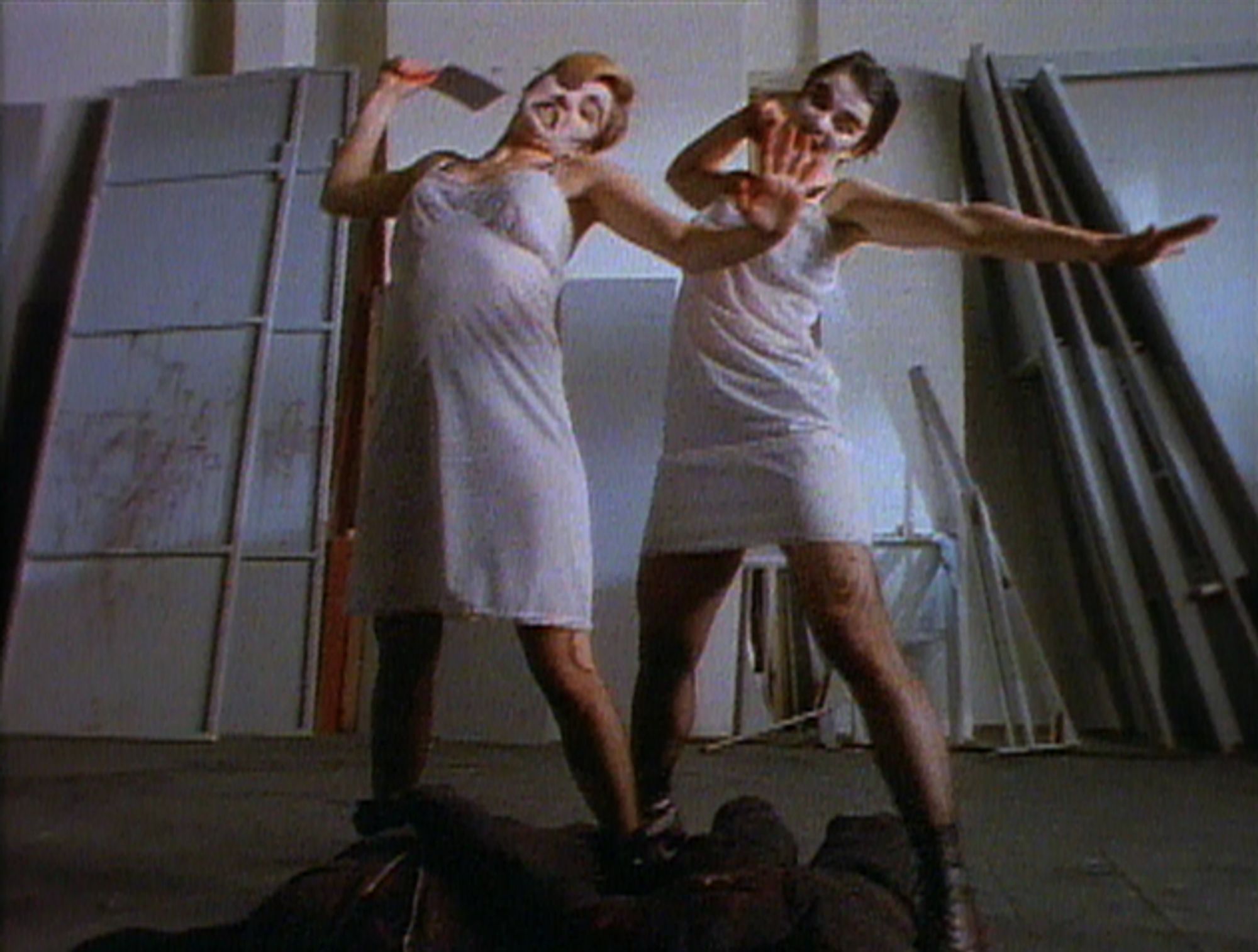 Two people wearing white dresses hold up a cleaver manically, ready to use it.