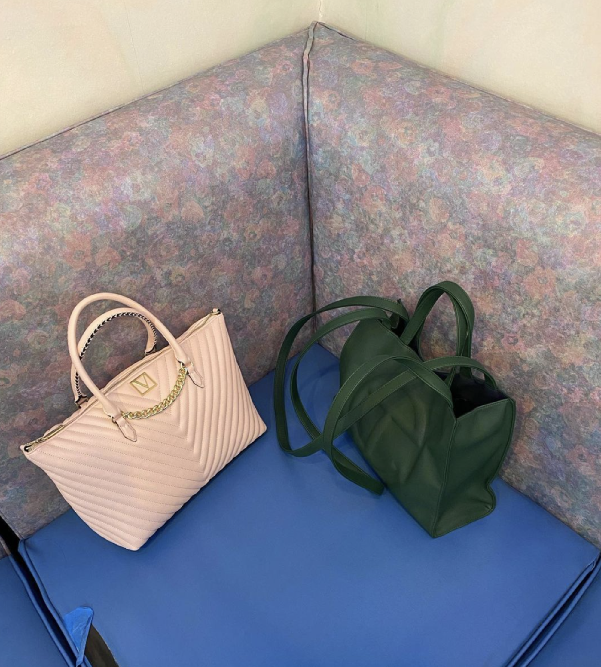 Two bags—one pastel pink purse, and a dark green Telfar tote, lean against a speckled plastic couch.