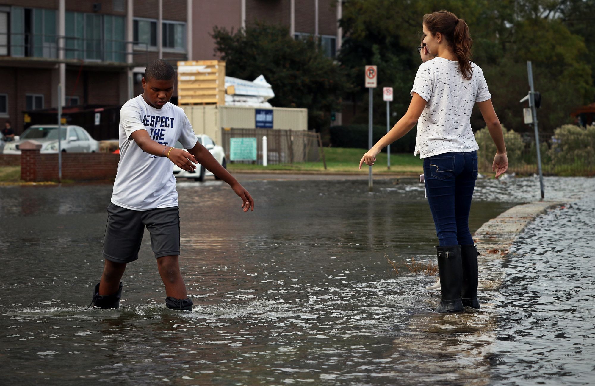 Three teenagers wade through flooded street 